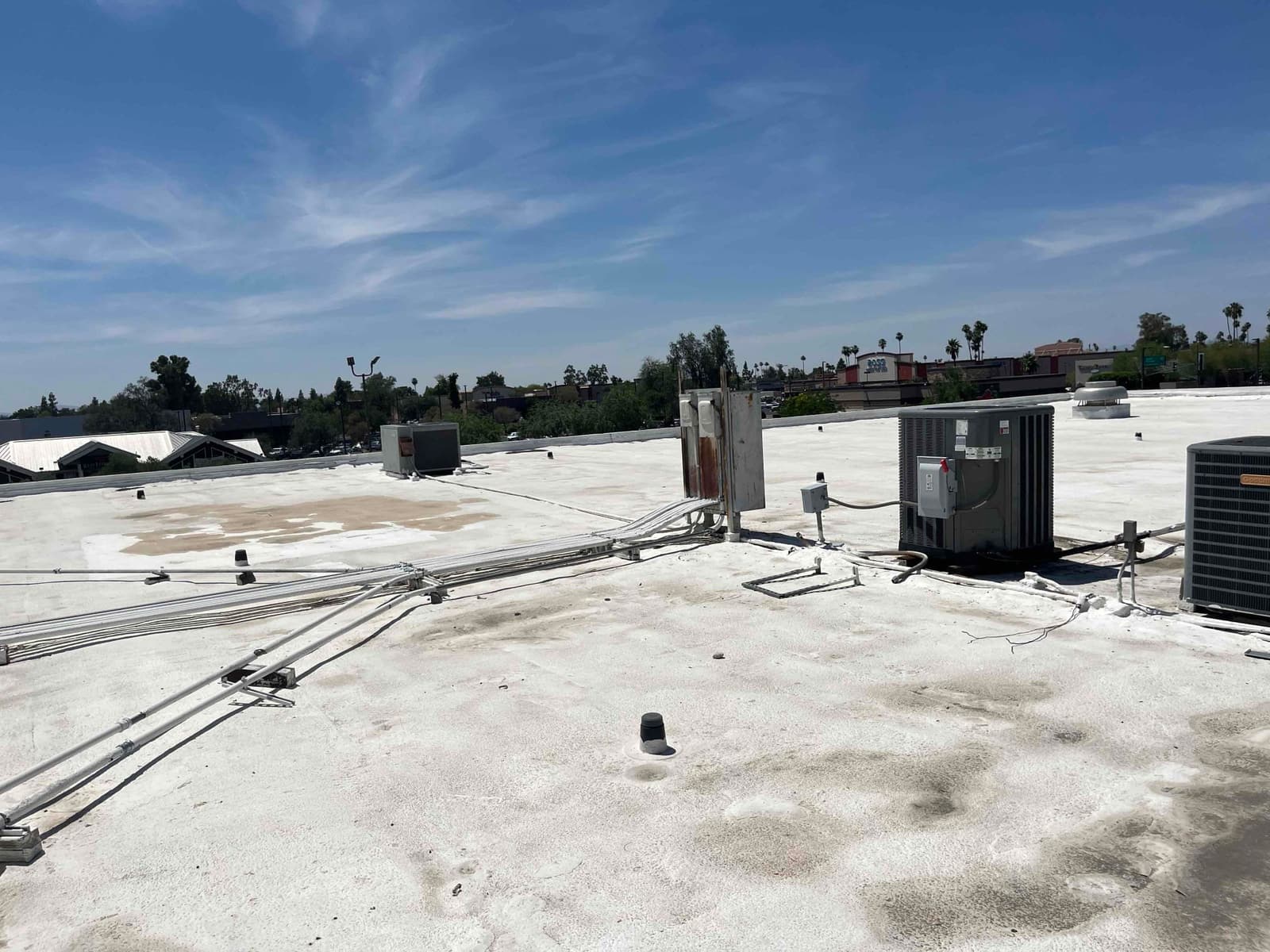 Multiple rooftop air conditioning condenser units and electrical conduits on a flat commercial roof under clear daytime conditions.