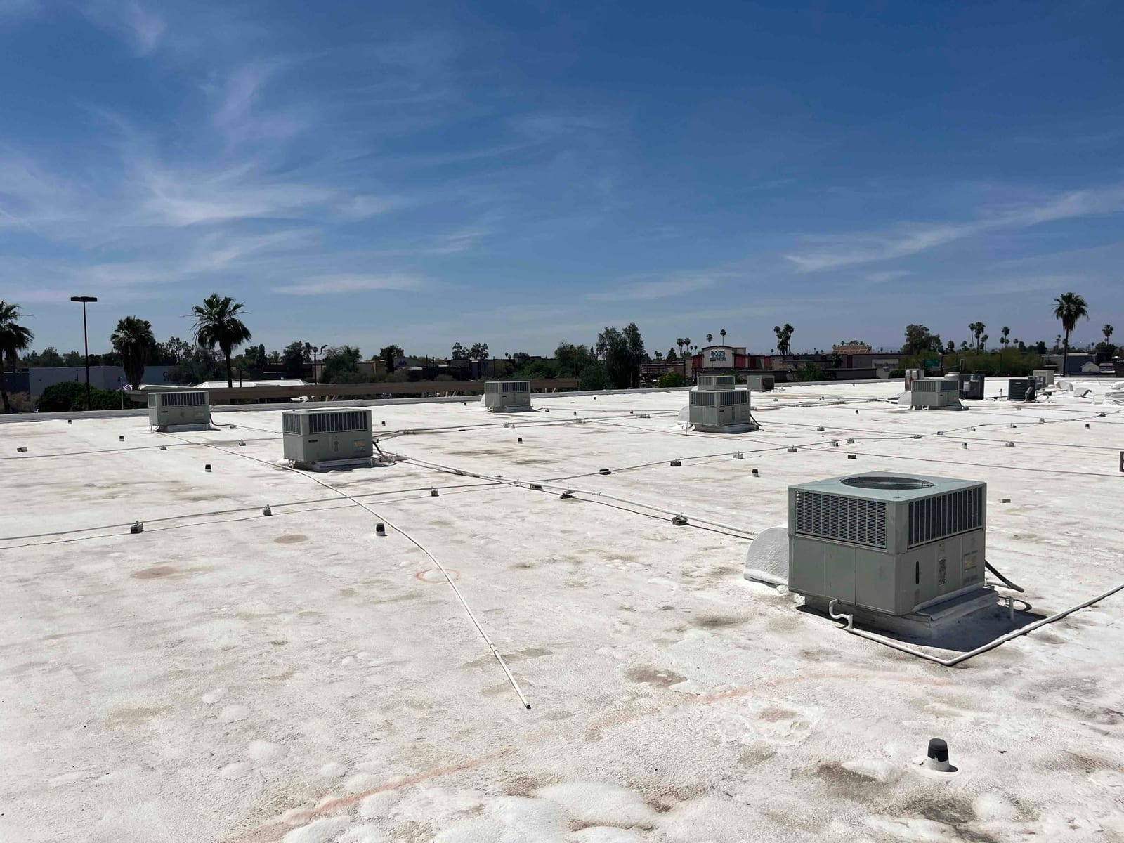 Multiple rooftop air conditioning condenser units spread across a flat roof, with electrical conduits and service disconnects visible.