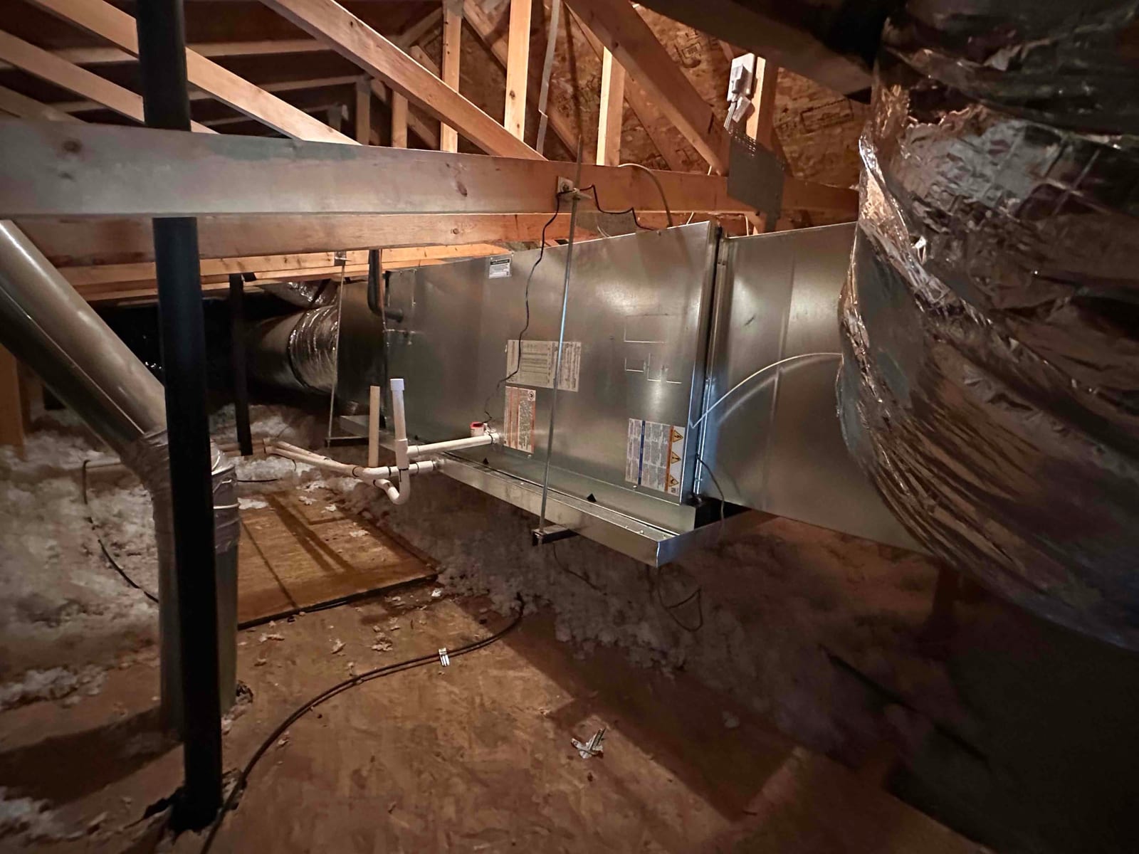 New attic air handler with sheet metal plenum, insulated flex ducts, and PVC condensate drain piping installed on a framed platform.