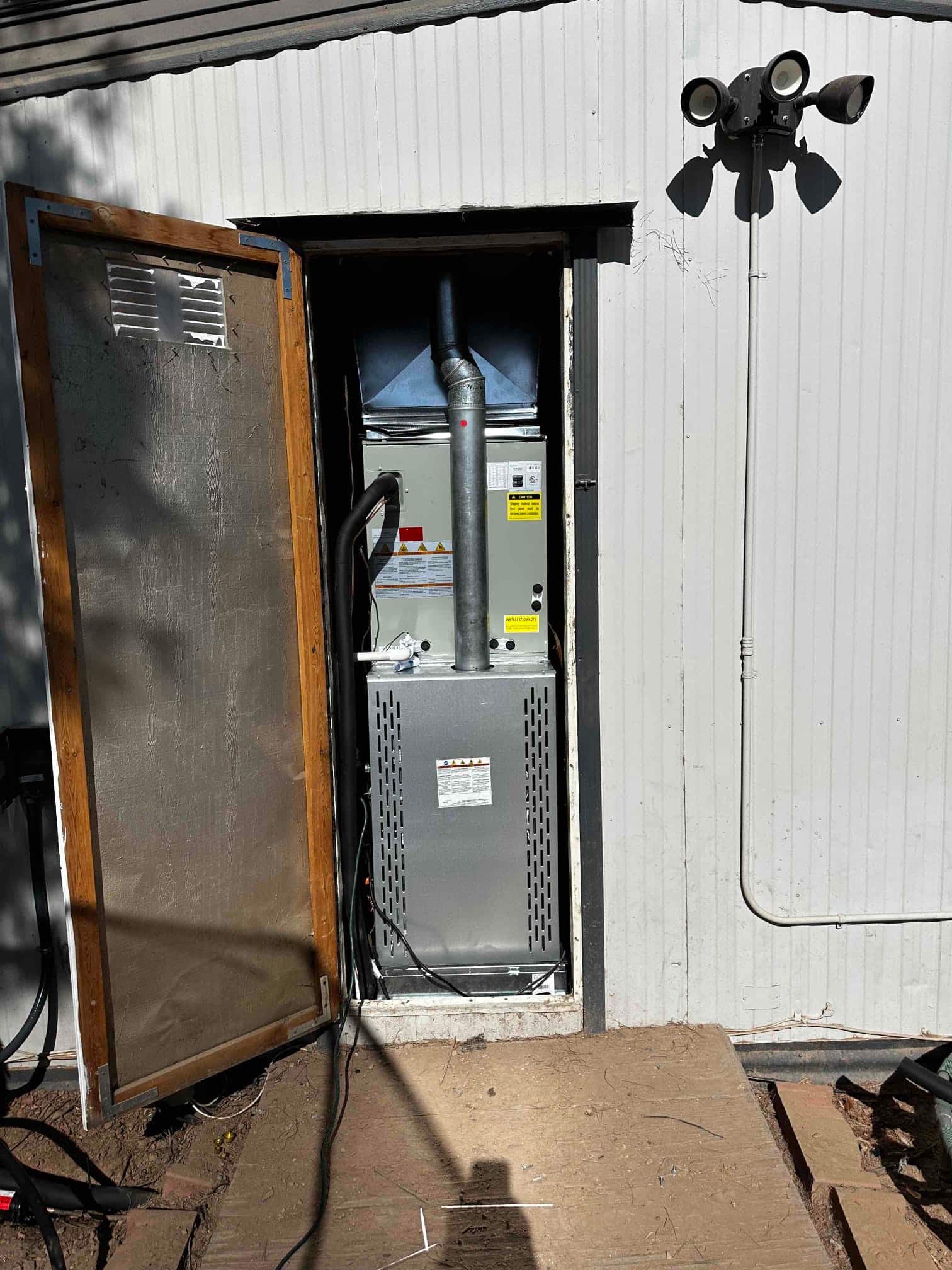 New gas furnace and evaporator coil installed in exterior closet with venting, insulated refrigerant line, and service access door open.