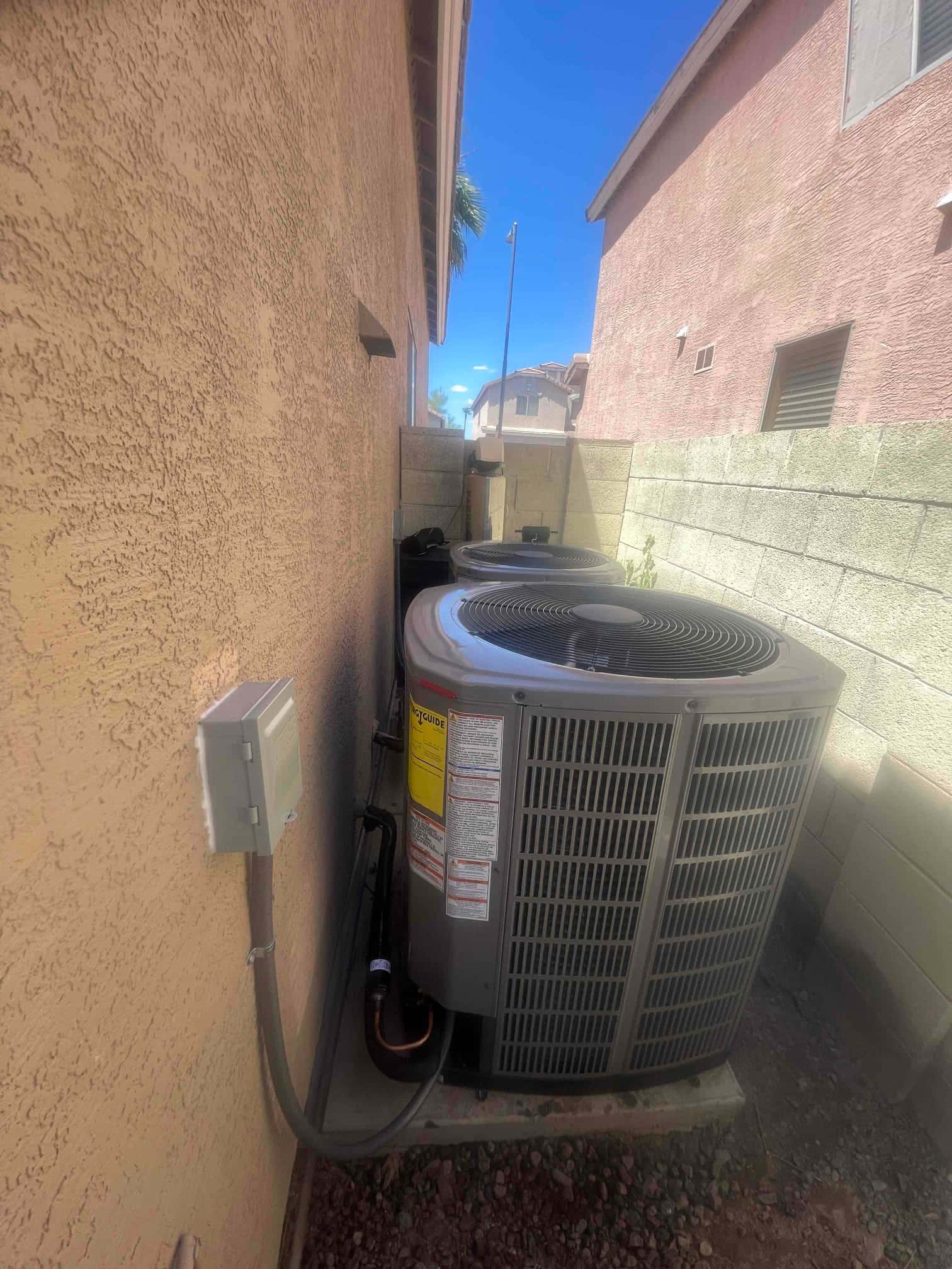 New outdoor condenser set on a concrete pad with insulated refrigerant lines and a wall-mounted electrical disconnect nearby.