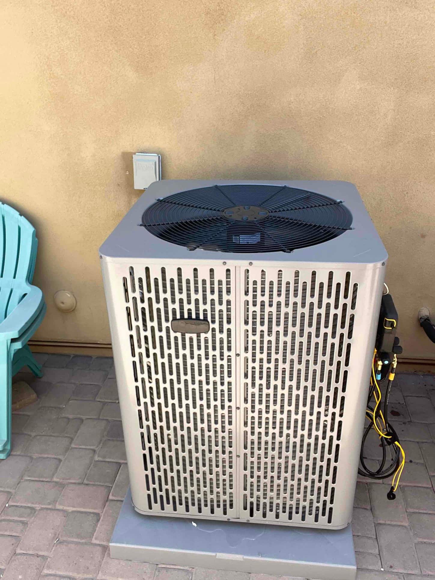 New outdoor condenser set on a level pad with nearby electrical disconnect and gauge hoses staged for commissioning.