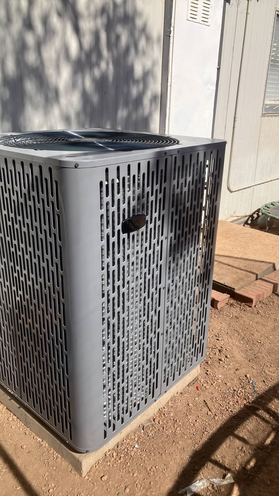 New outdoor condenser set on a level pad next to the building, with protective grille and coil cabinet in place.