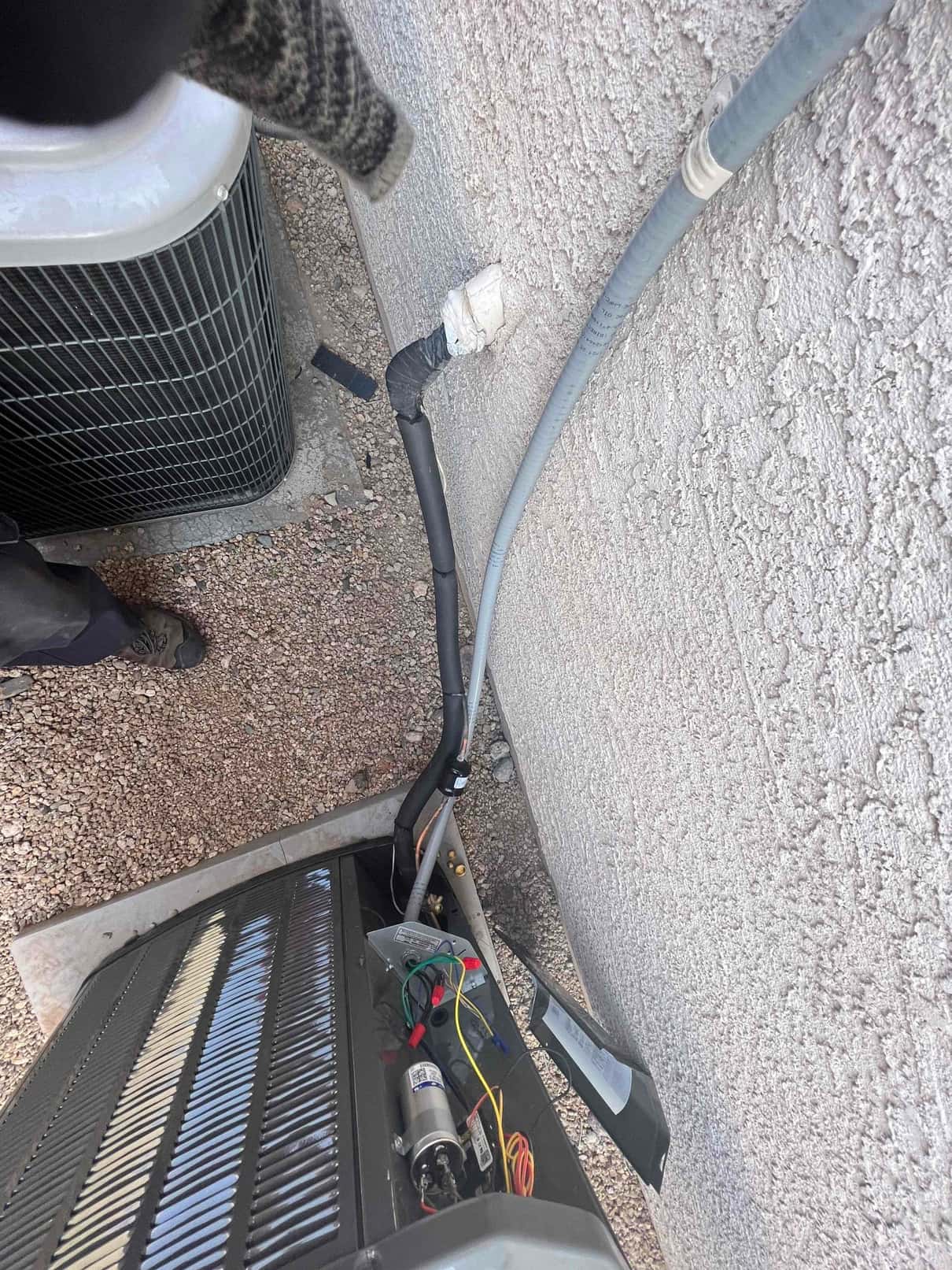 New outdoor condenser set on a pad with insulated refrigerant line set and electrical whip routed along the wall.