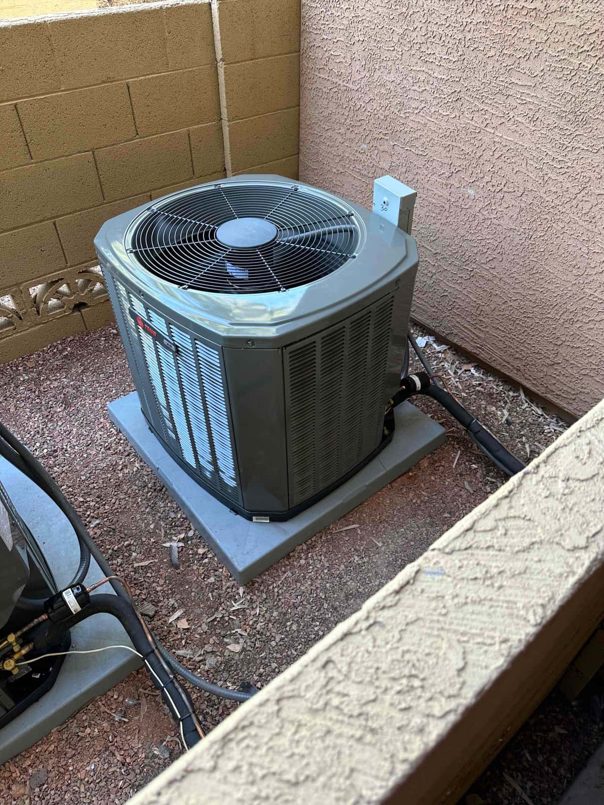 New outdoor heat pump condenser set on a level pad with insulated refrigerant lines and exterior disconnect mounted nearby.