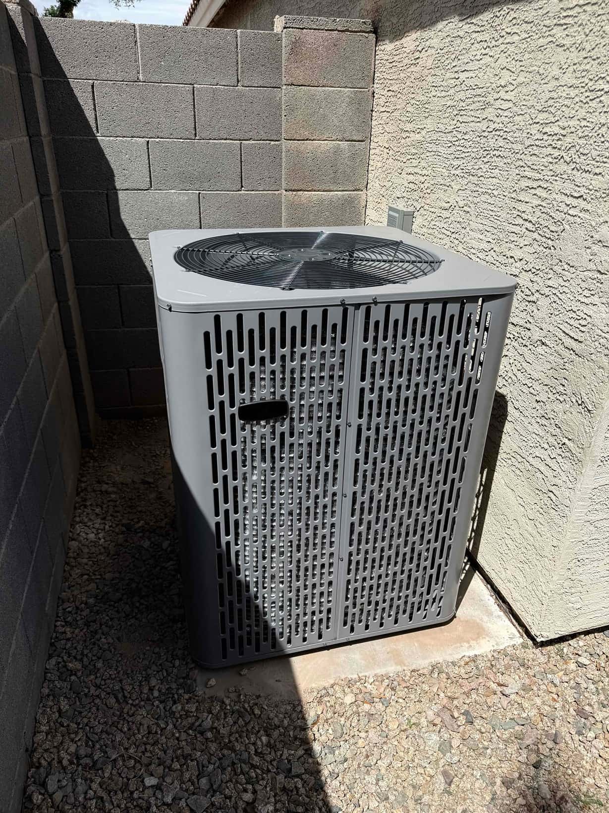New outdoor heat pump condenser set on a level pad within a side yard enclosure, with top discharge fan and protective grille.