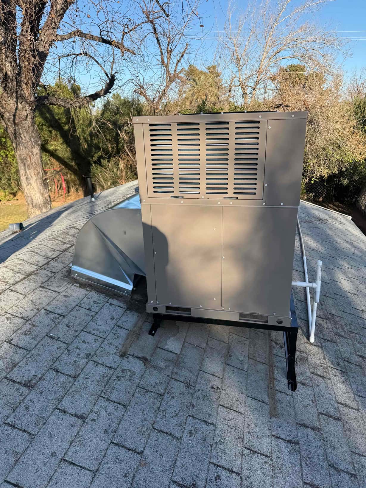 New rooftop package HVAC unit set on a metal stand with connected duct transition and condensate drain piping.