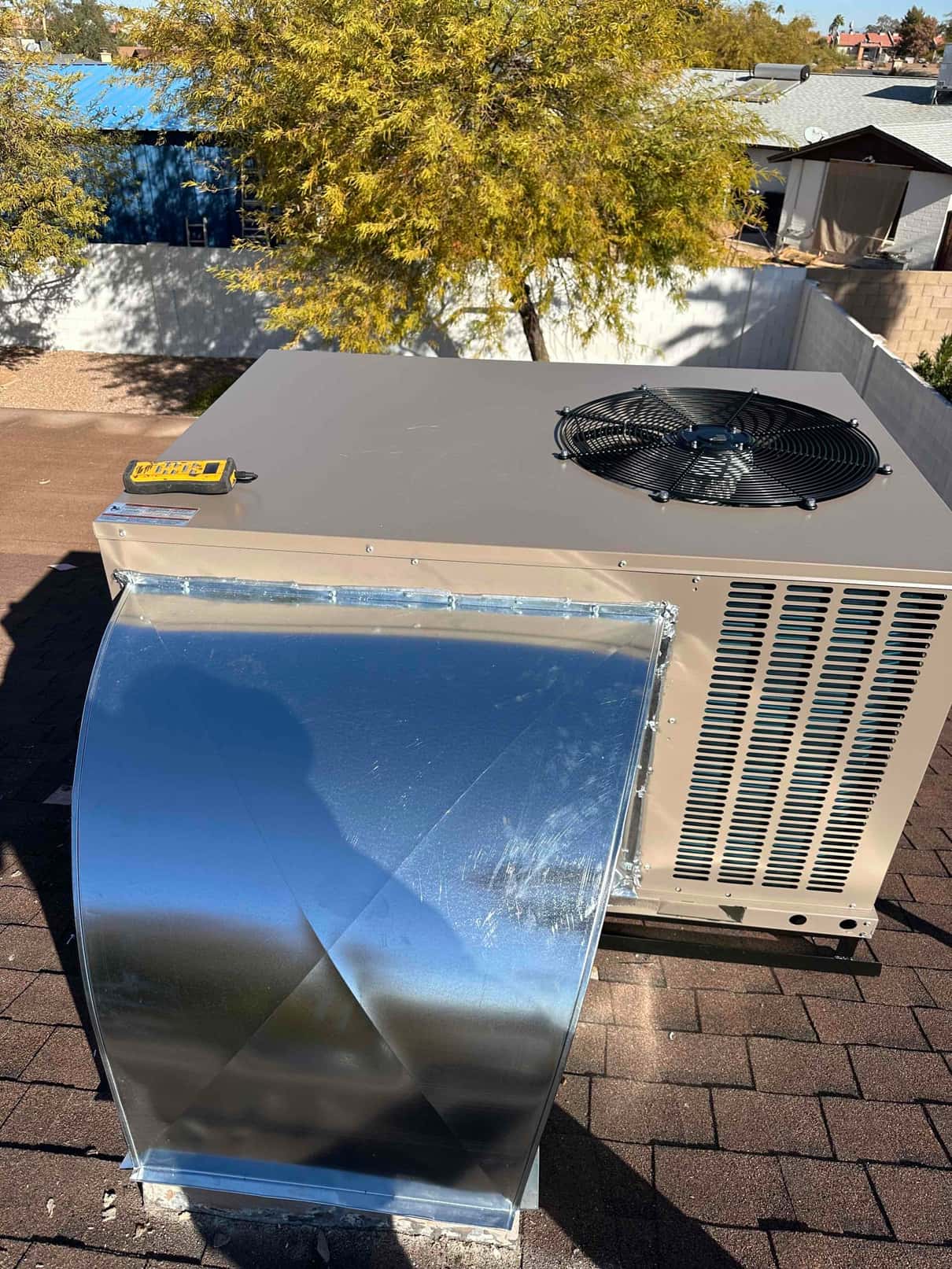 New rooftop package unit installed with sealed sheet metal transition on curb, condenser fan visible on top panel.