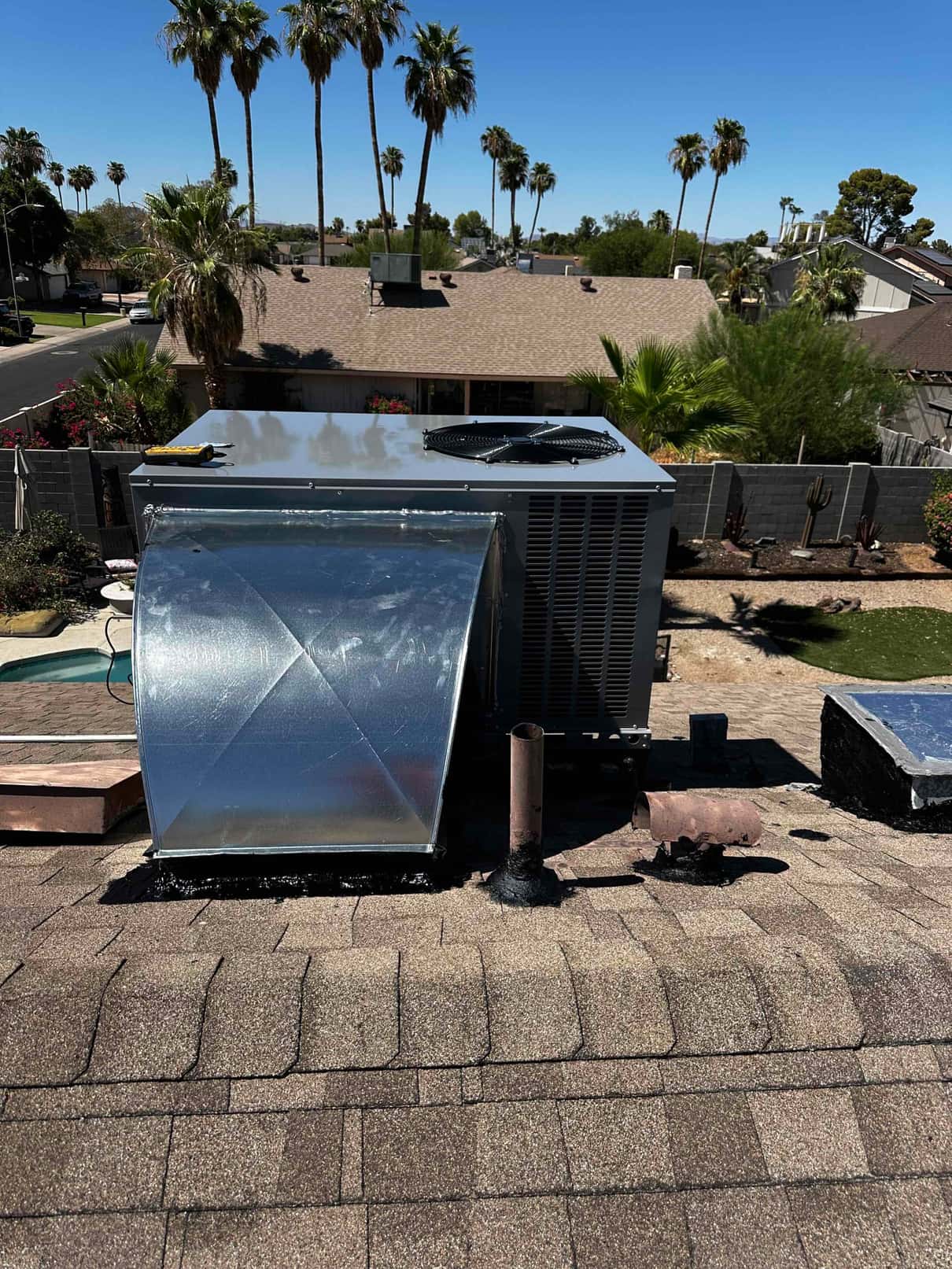 New rooftop package unit installed on shingles with sealed curb and metal transition duct connected, viewed from the roof ridge.