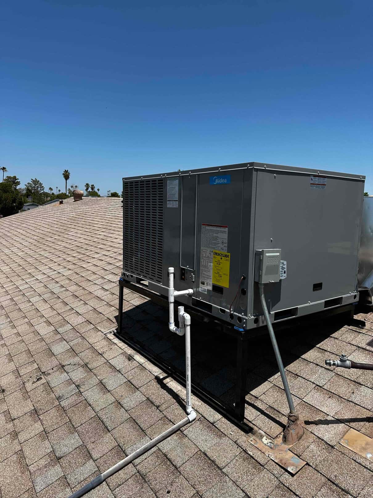 New rooftop package unit mounted on a metal stand with installed condensate drain piping and electrical disconnect in place.