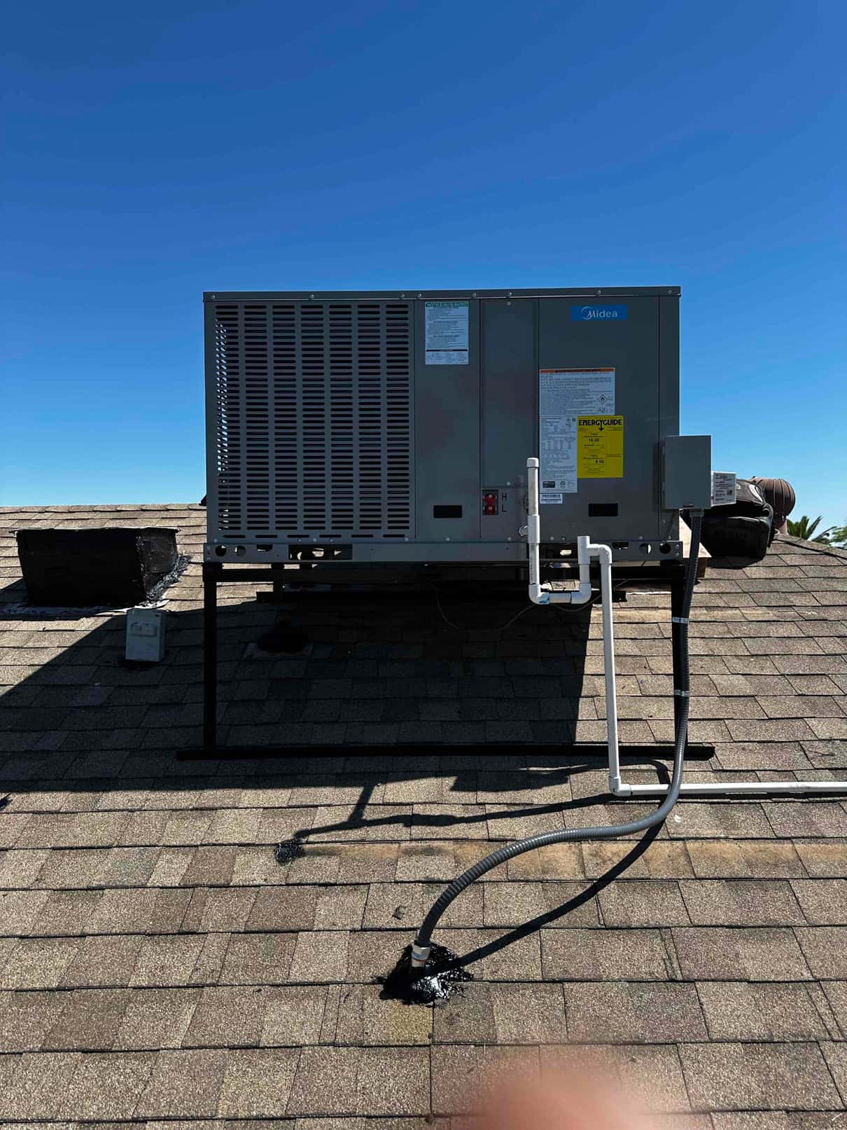 New rooftop package unit set on a raised stand with sealed roof penetrations, electrical whip, and condensate drain piping routed.