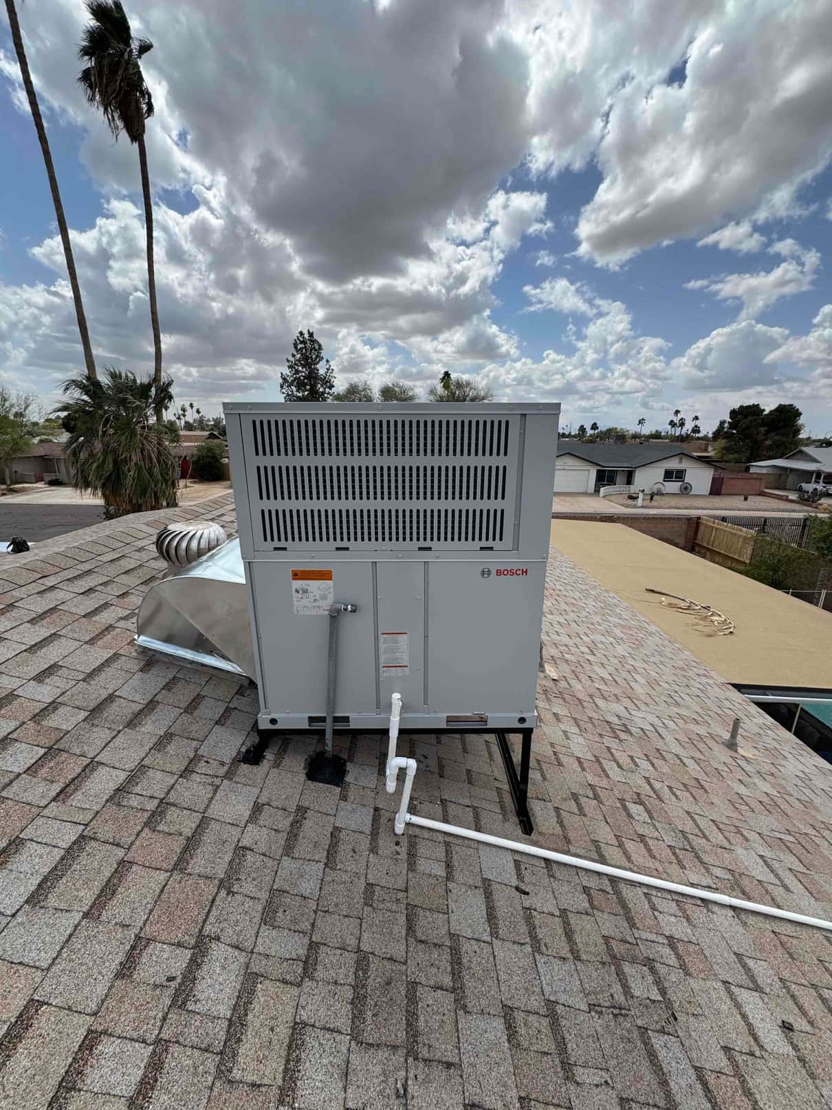 New rooftop packaged heat pump set on a metal stand with connected duct transition and insulated condensate drain piping.