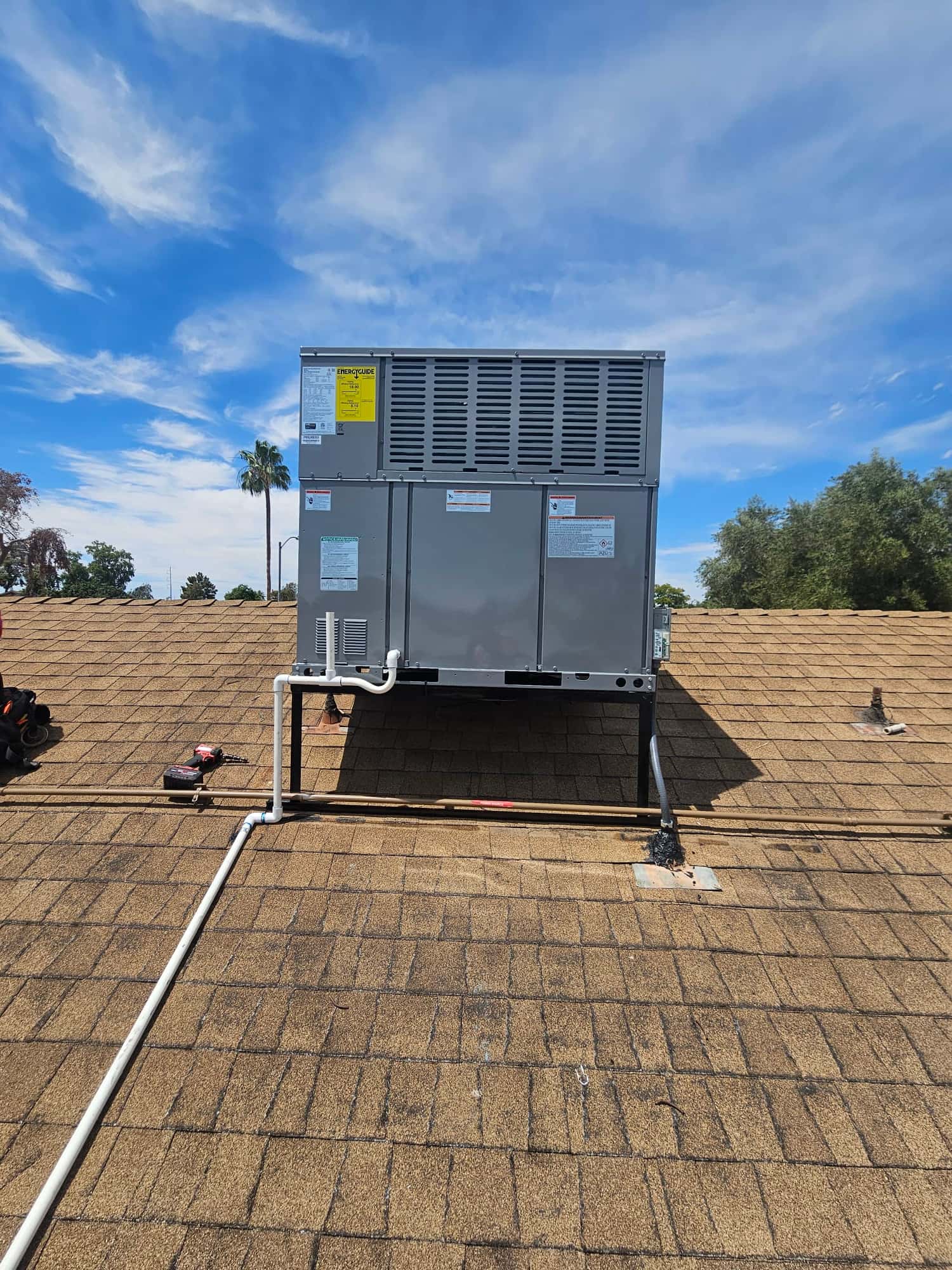 New rooftop packaged HVAC unit mounted on stands with insulated condensate drain and electrical conduit routed across the shingle roof.