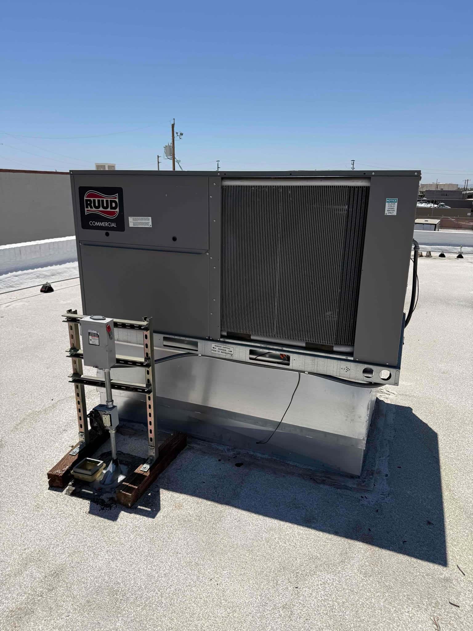 New rooftop packaged unit set on a curb with electrical disconnect mounted on support rails and sealed roof penetration.