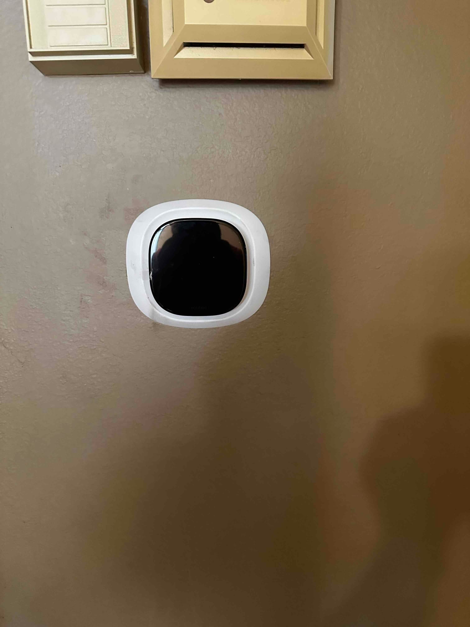 New wall-mounted thermostat installed below existing control devices, centered and neatly finished for the HVAC system.