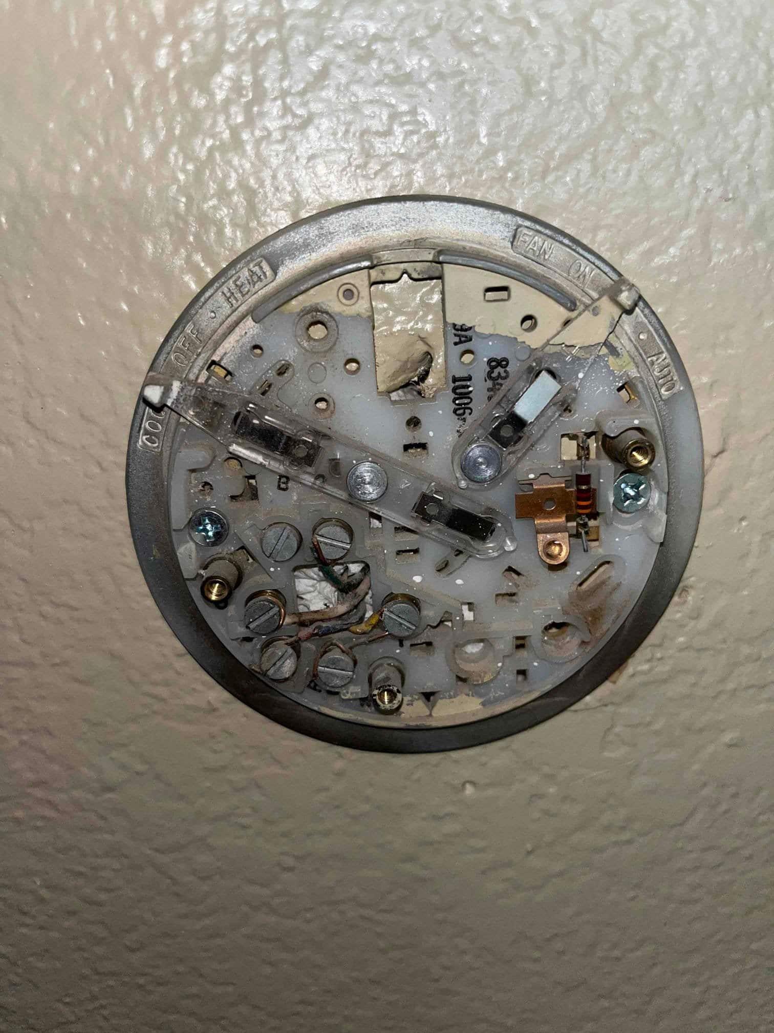 Old round thermostat base on wall with exposed low-voltage terminals, wiring, and mechanical switch components visible.