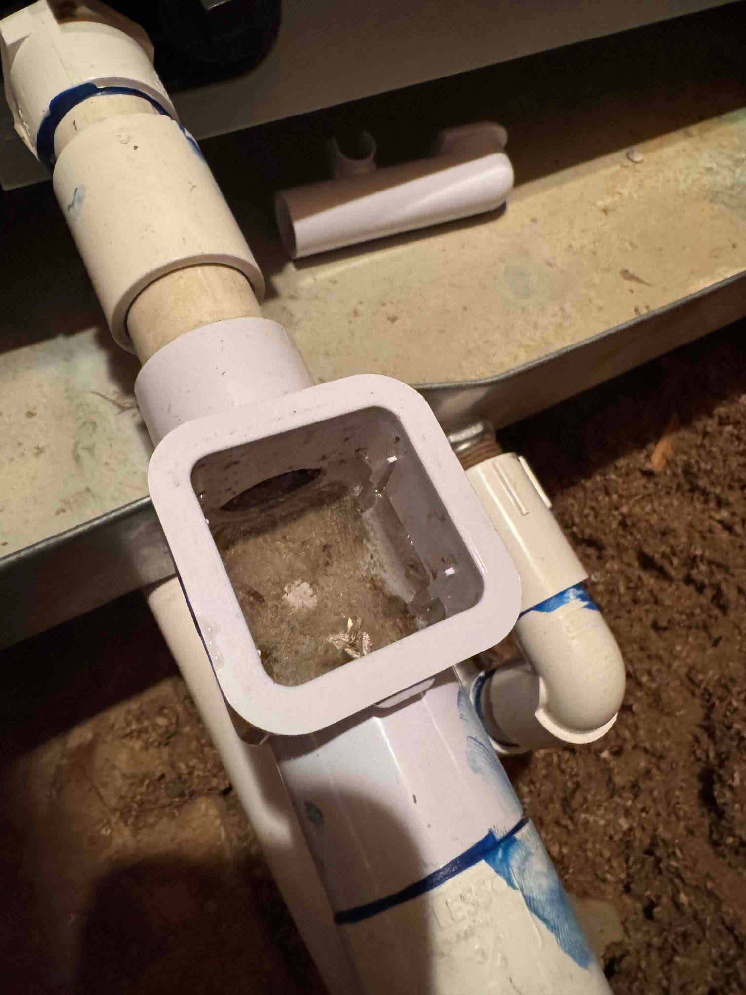 Open condensate drain cleanout shows accumulated debris and sludge inside PVC fitting before cleaning during drain line repair.