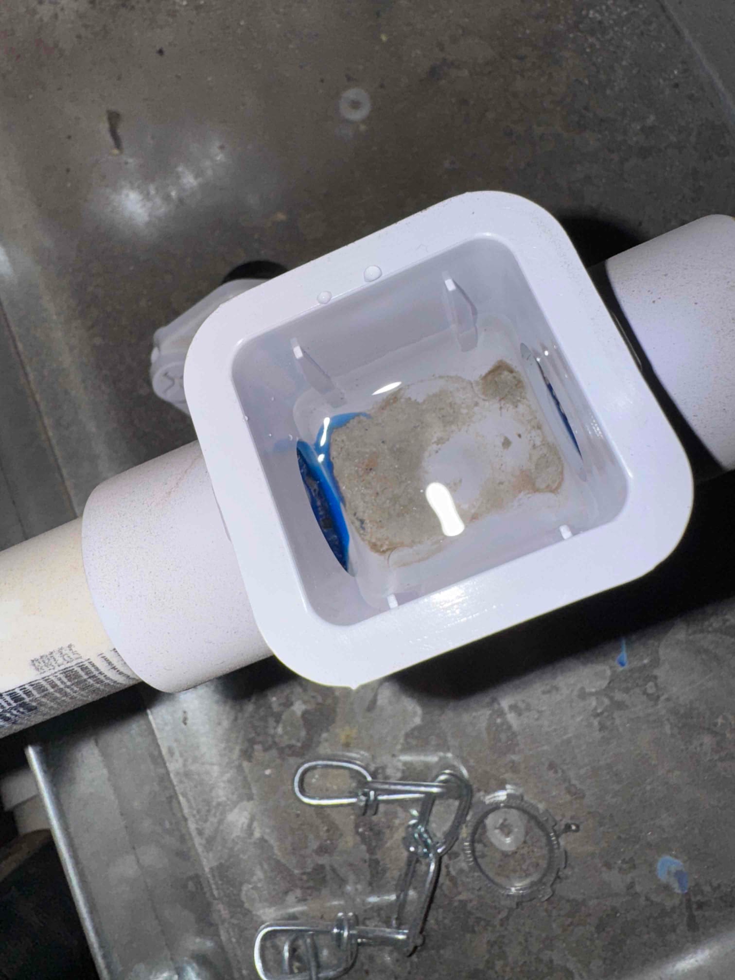 Open condensate drain cleanout shows standing water and sediment inside PVC drain assembly during repair.
