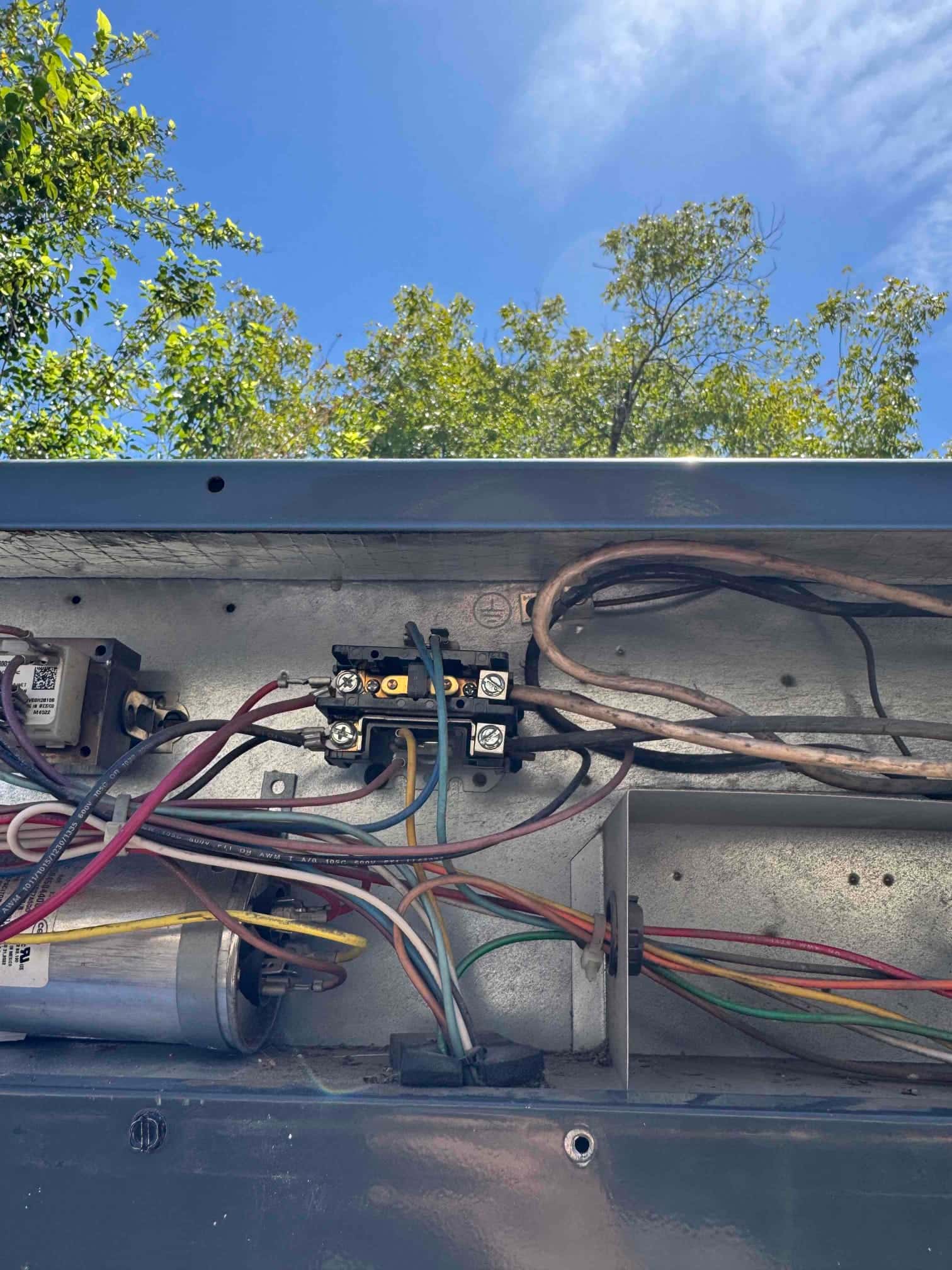 Open condenser control compartment showing contactor, run capacitor, and multiple control wires routed through the housing.
