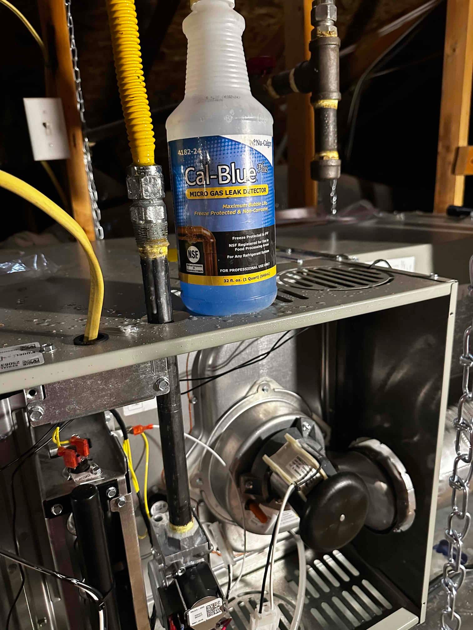 Open furnace cabinet shows gas piping, condensate trap, and inducer assembly, with leak detector solution bottle resting on the top panel.