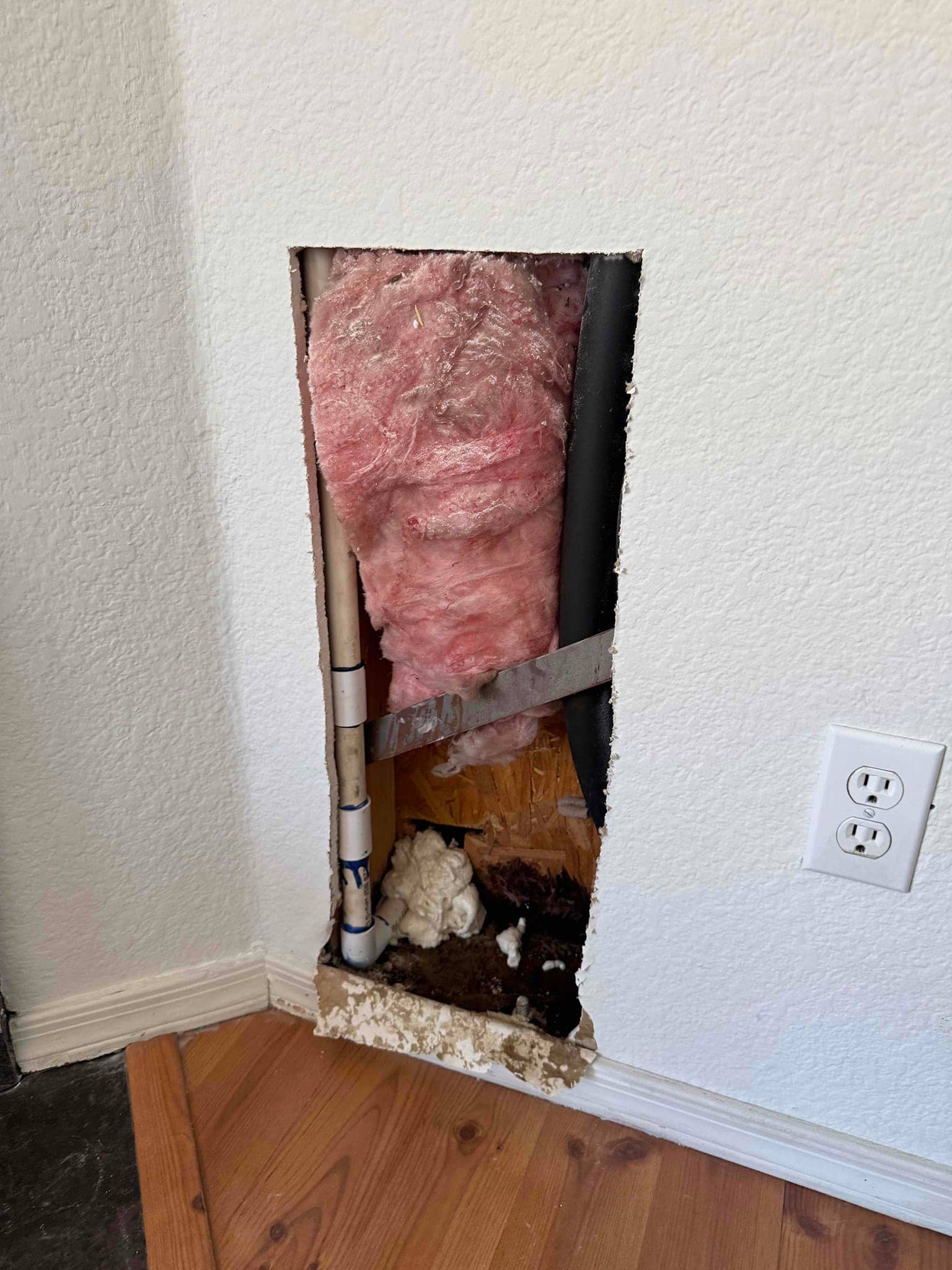 Open wall access shows condensate drain line with PVC fittings, surrounding insulation, and water-damaged debris at the wall base.