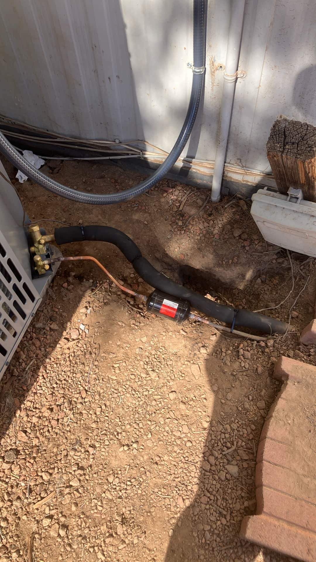 Outdoor condenser connections with insulated suction line, liquid line with inline filter-drier, and secured condensate drain routing against the wall.
