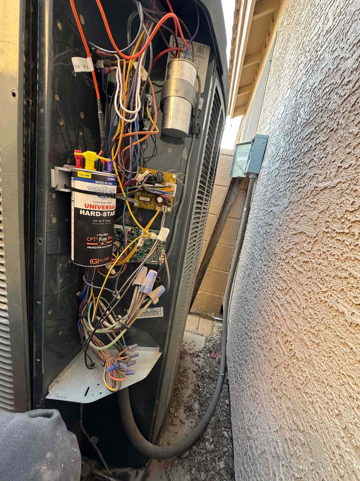 Outdoor condenser control compartment open, showing installed universal hard-start kit and dual-run capacitor with connected wiring and contactor.