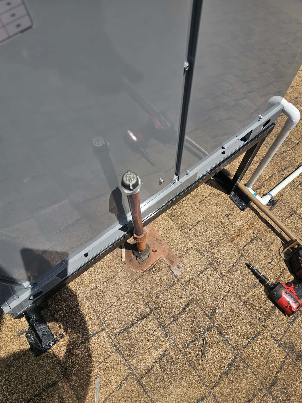 Outdoor condenser mounted on a rooftop stand with nearby vent penetration and tools visible during installation work.