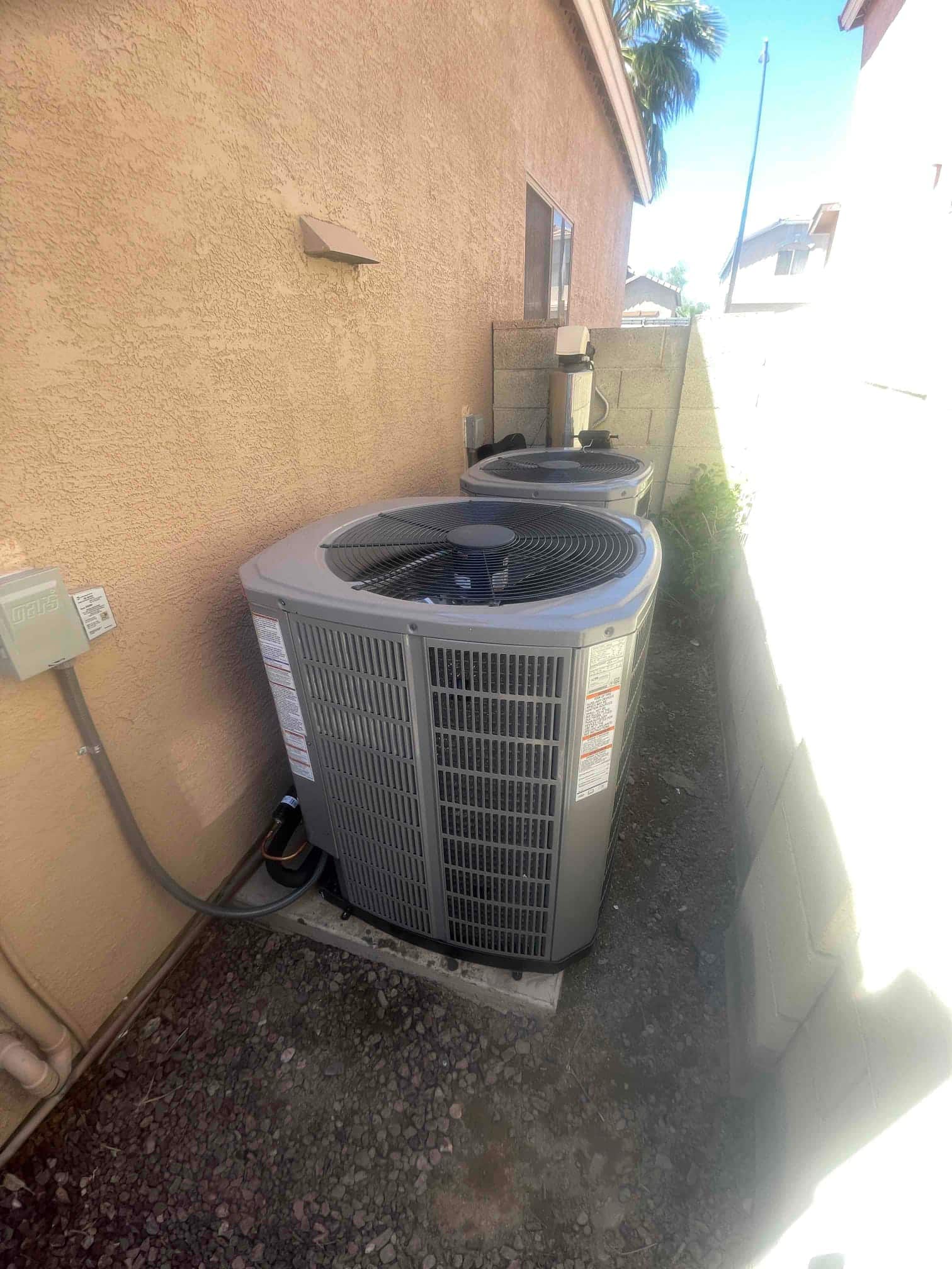 Two outdoor condensers set on level pads along the side yard, with insulated refrigerant lines and electrical disconnects mounted nearby.