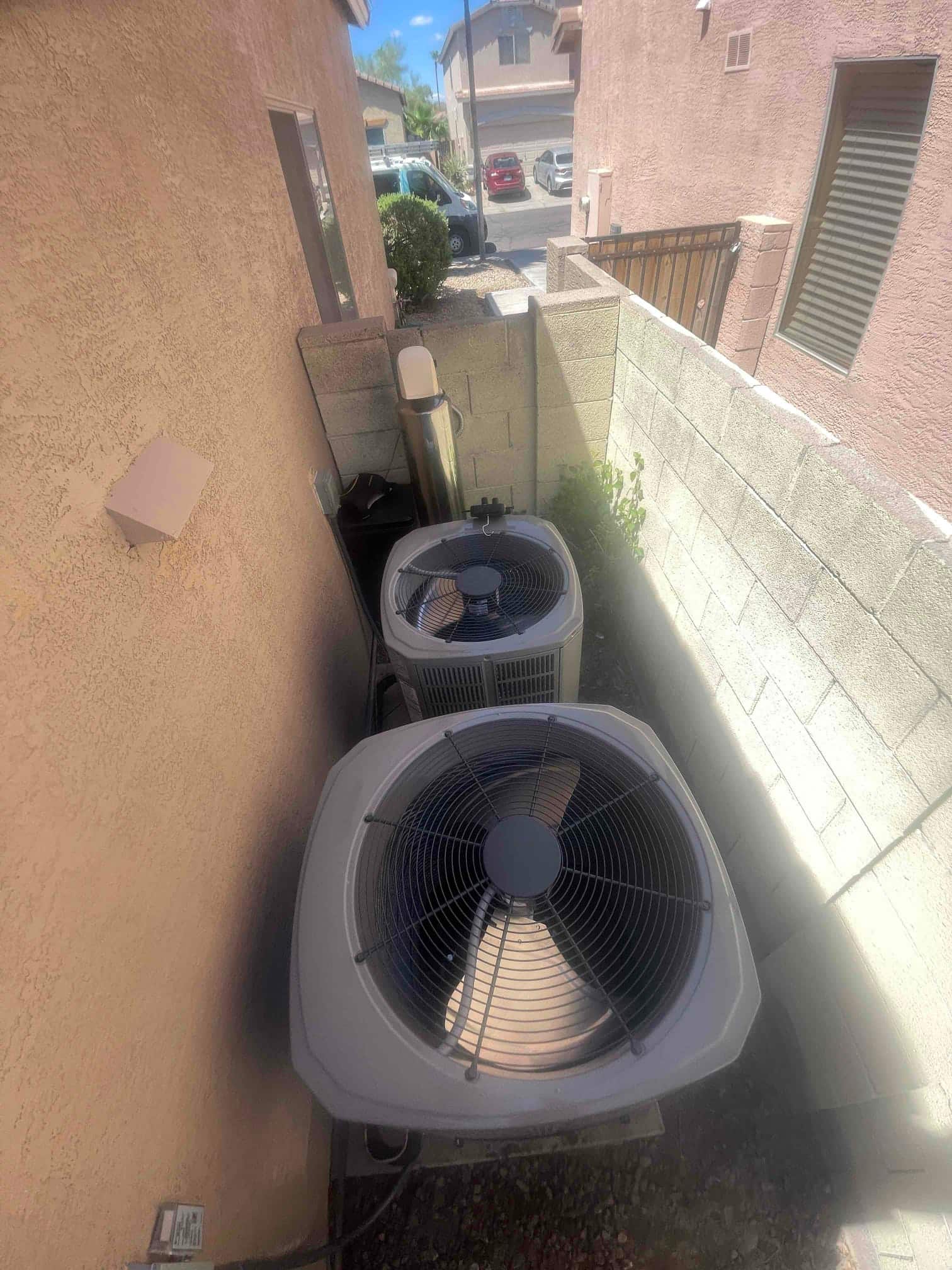 Two outdoor condensers set on pads in a narrow side yard, connected to refrigerant lines and electrical whip.