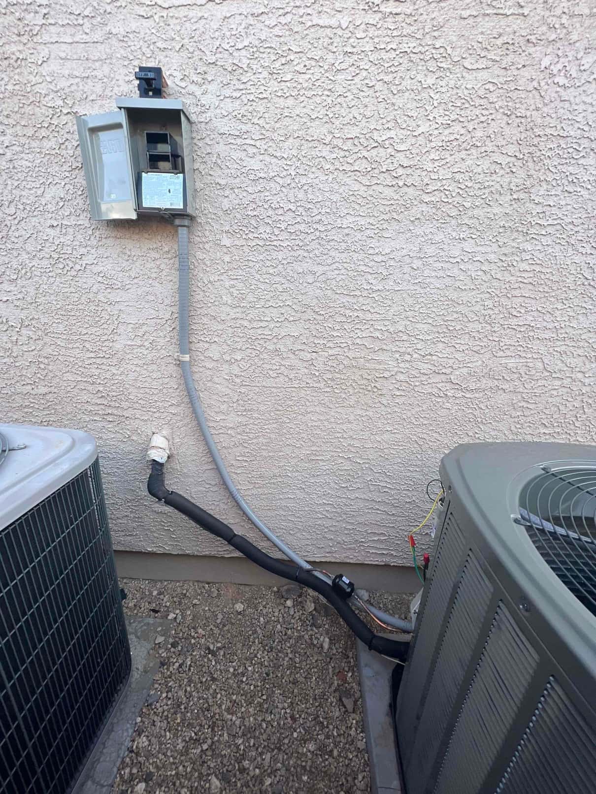 Outdoor condensers set on pads with new disconnect, sealed wall penetration, and insulated refrigerant line set routing.