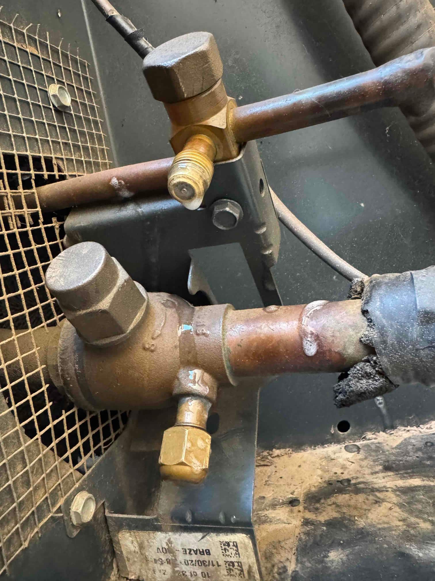 Outdoor condensing unit service valves and refrigerant lines, showing schrader access ports and insulation with visible wear at the suction line.