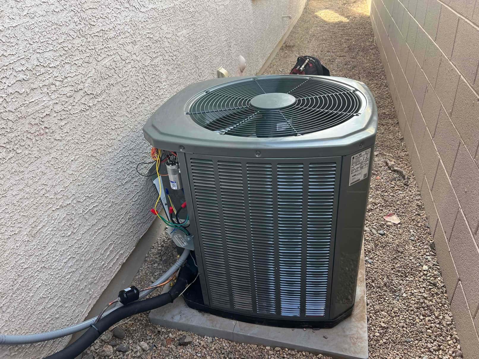 Outdoor condensing unit set on a level pad with insulated line set, wiring connections open for installation work.