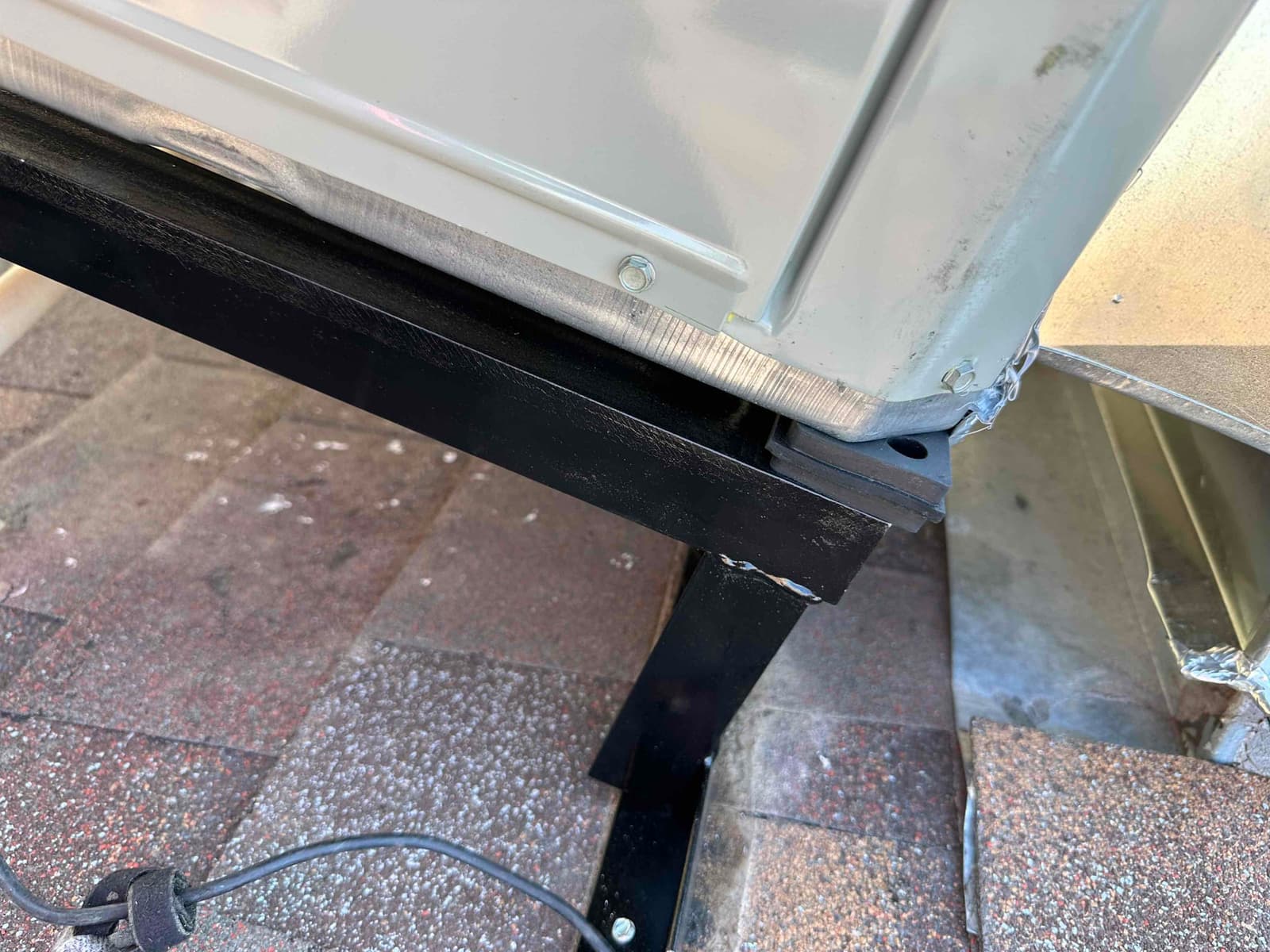 Package HVAC unit corner secured on a rooftop curb stand with vibration isolation pad and flashing visible.