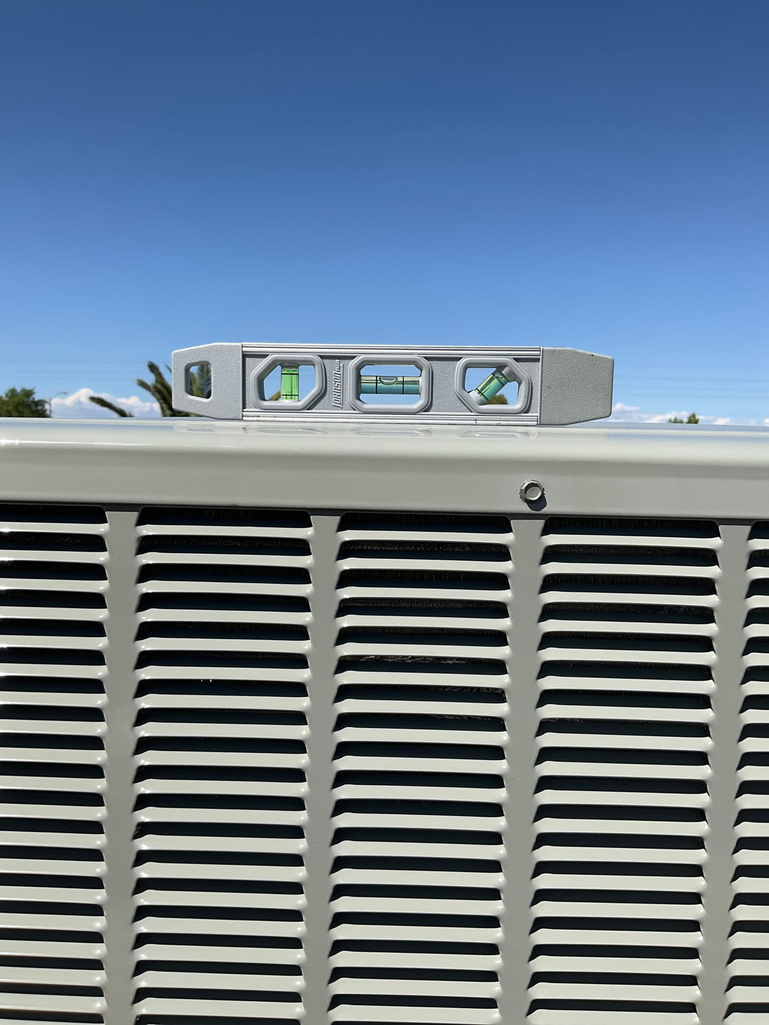 Bubble level placed on top of a newly installed outdoor HVAC package unit to verify the cabinet is set level.