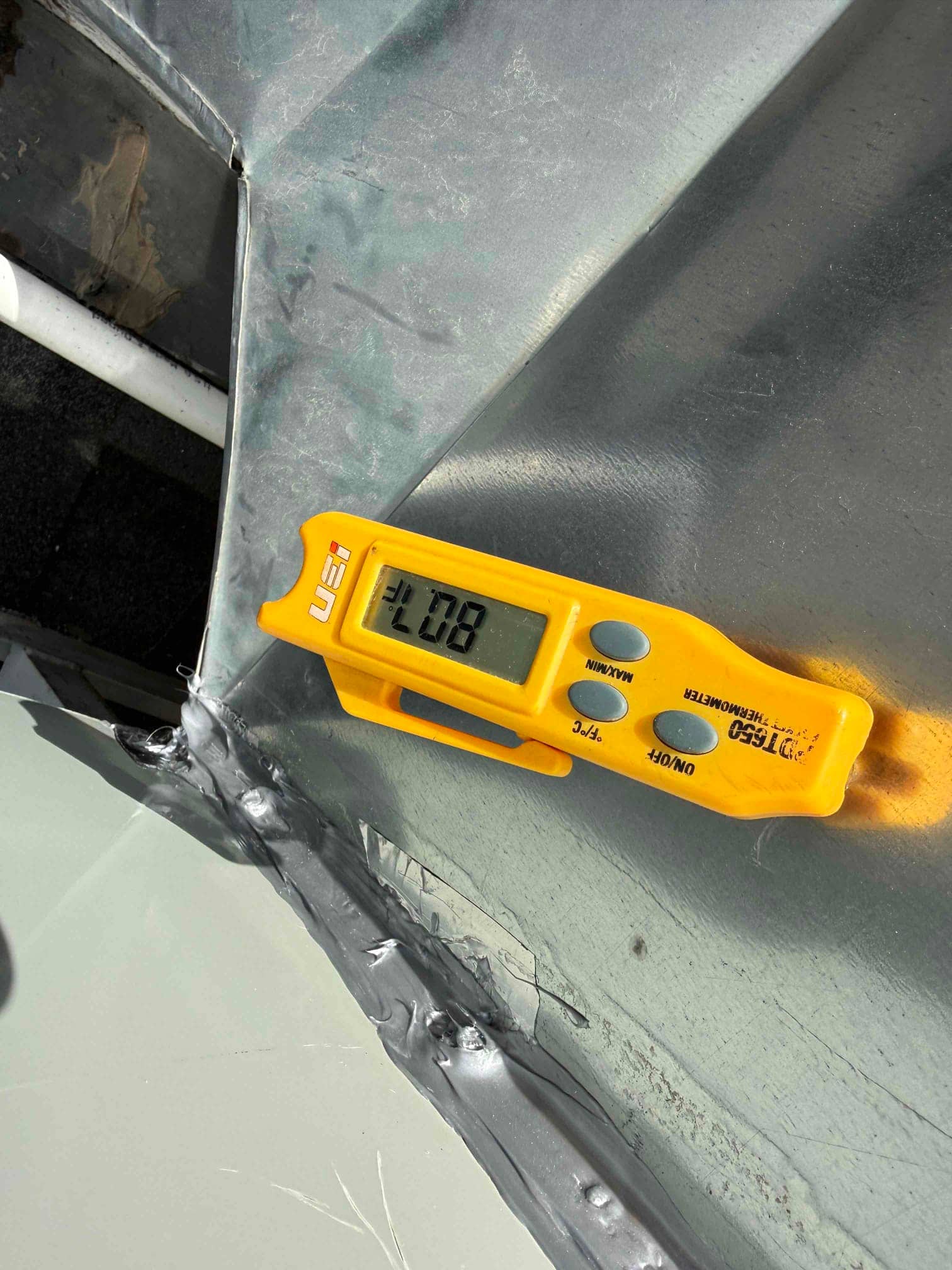 Digital thermometer inserted in ductwork reads 80°F during return air temperature check on the installed system.