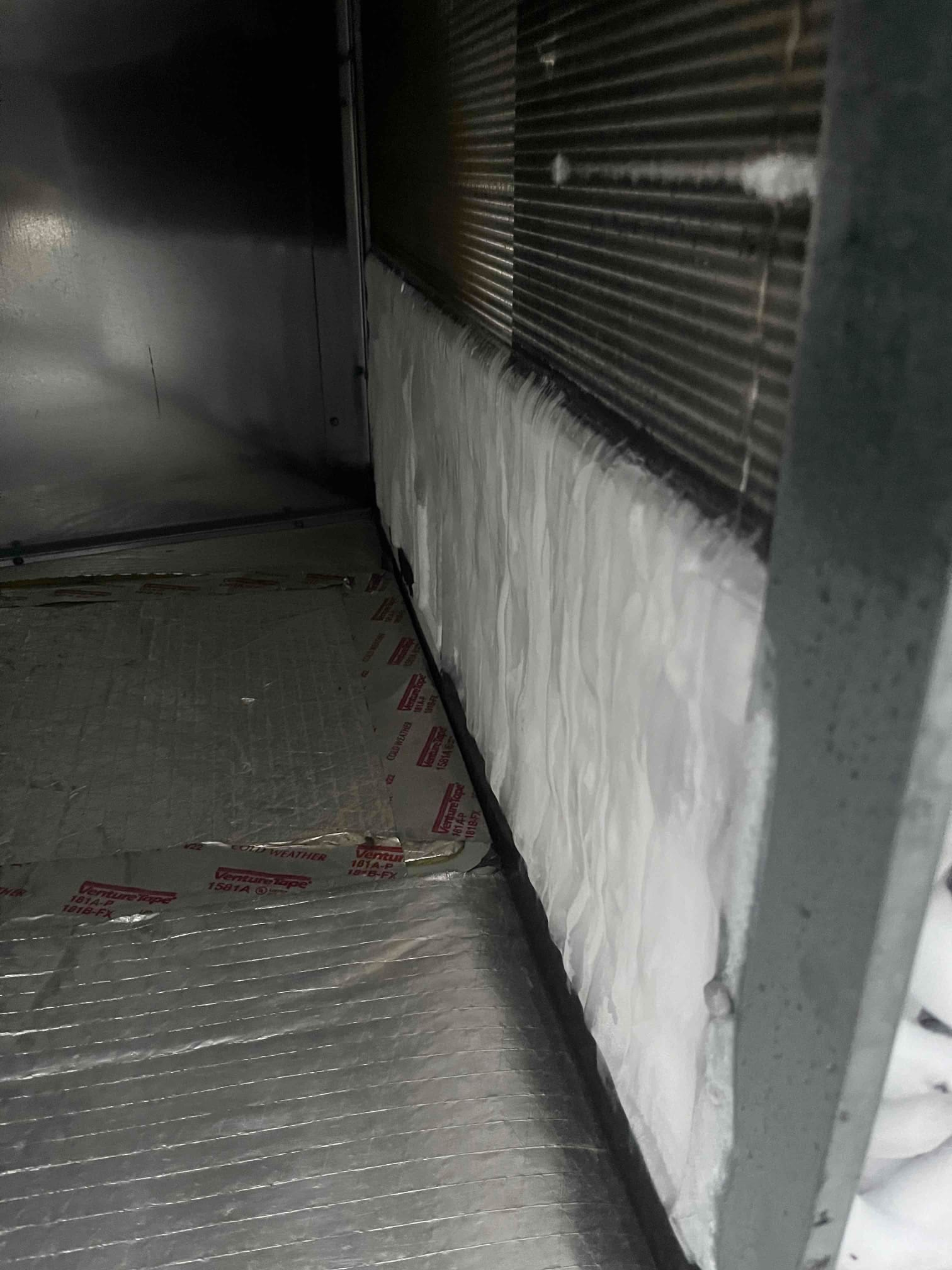 Evaporator coil section with heavy ice buildup along the lower fins and adjacent insulated panel inside the air handler.