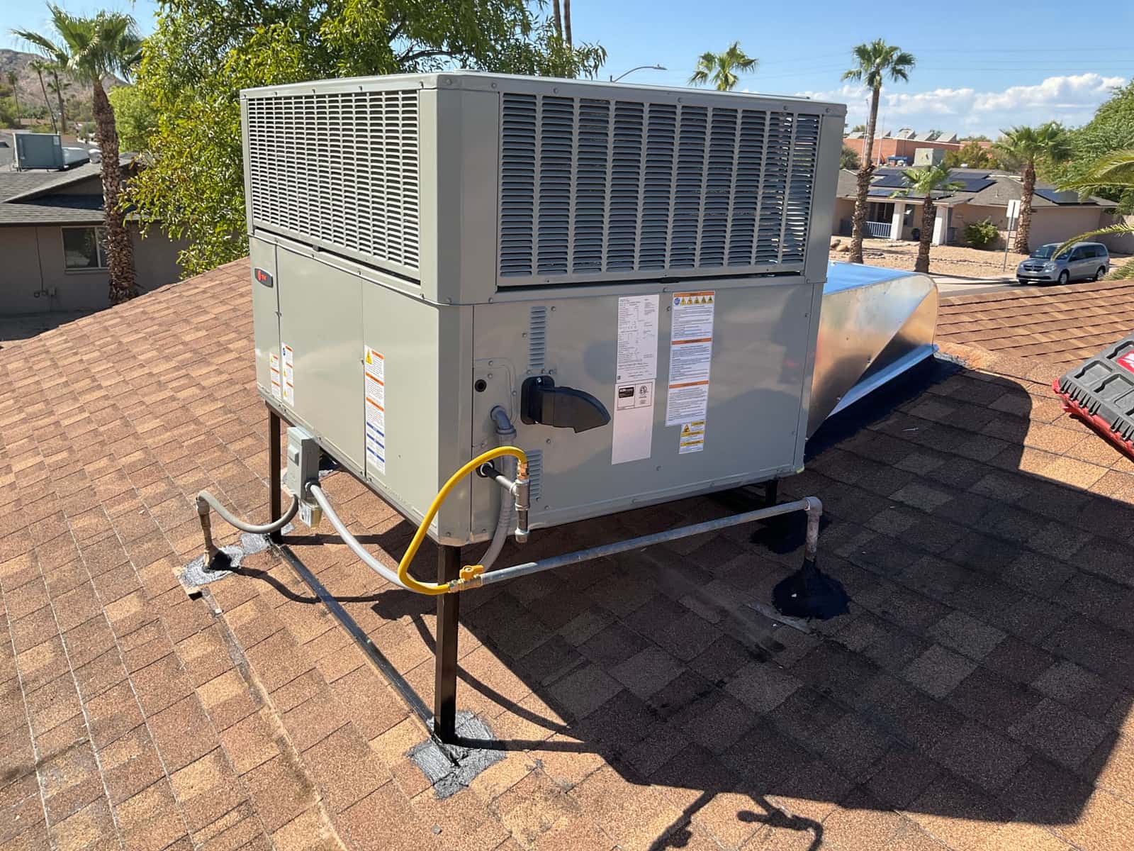 New rooftop package HVAC unit mounted on stands with sealed roof penetrations, gas piping, electrical disconnect, and curb adapter connected.