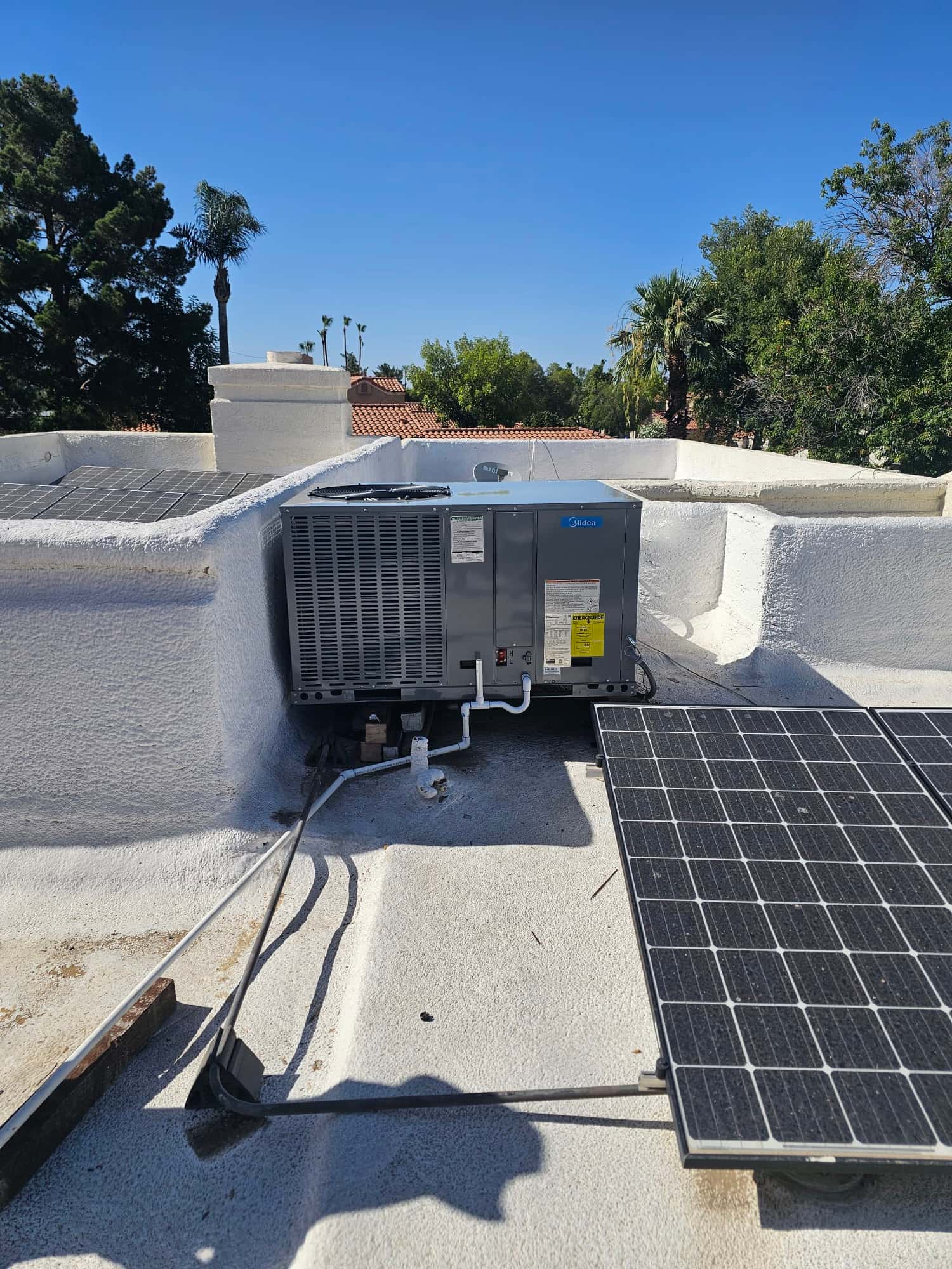 New rooftop package HVAC unit set on a coated roof with connected condensate drain and electrical whip alongside nearby solar panel.