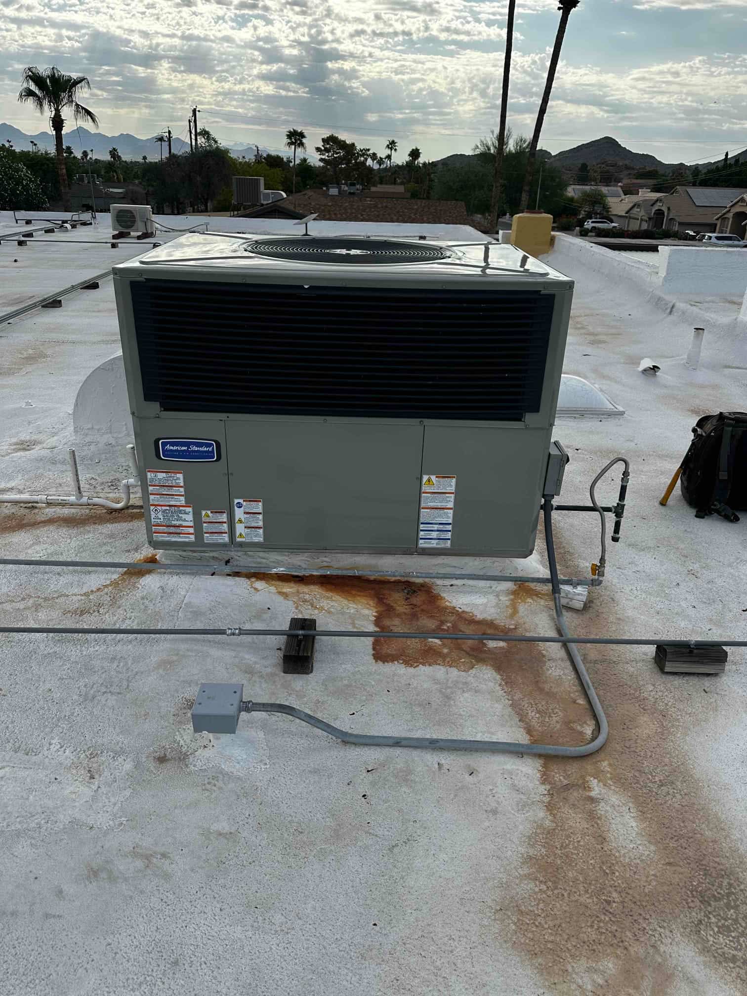 New rooftop package HVAC unit set on curb with electrical conduit and gas line connections visible on the service side.