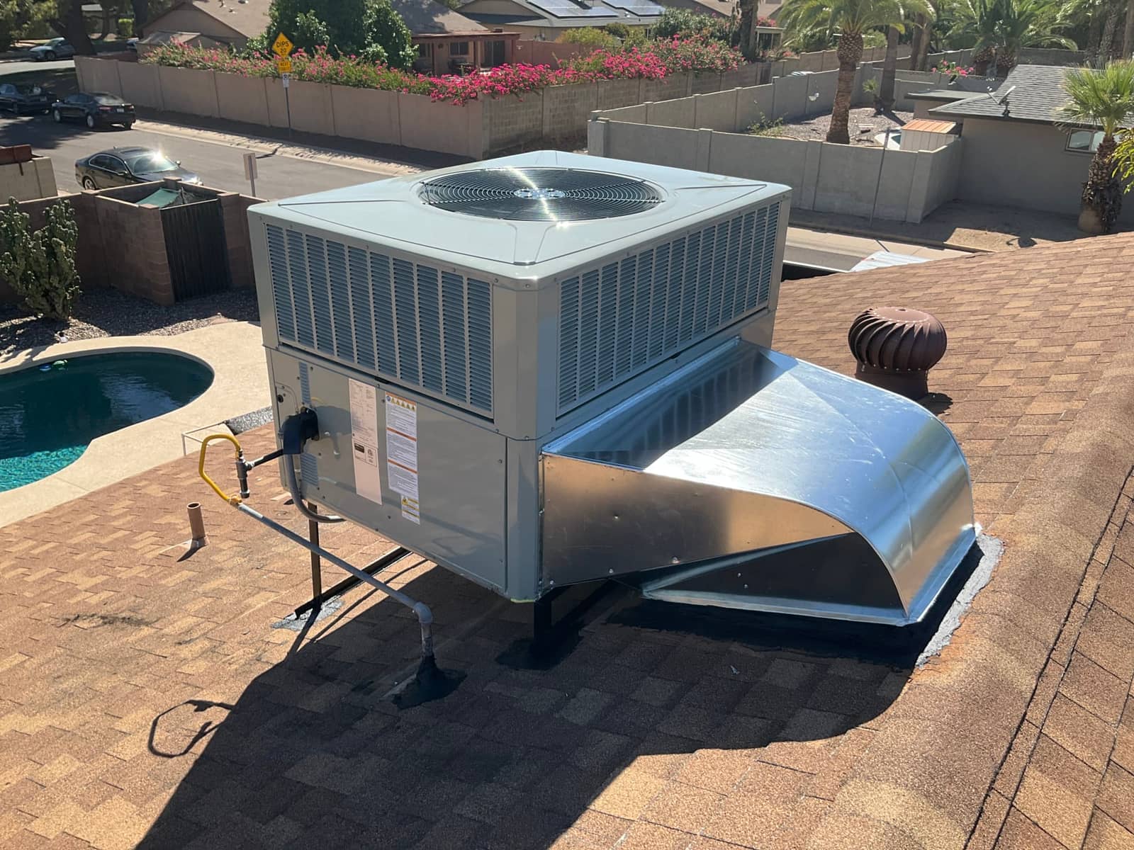 New rooftop package unit installed on curb with sealed supply plenum, gas line connection, and level supports on shingle roof.