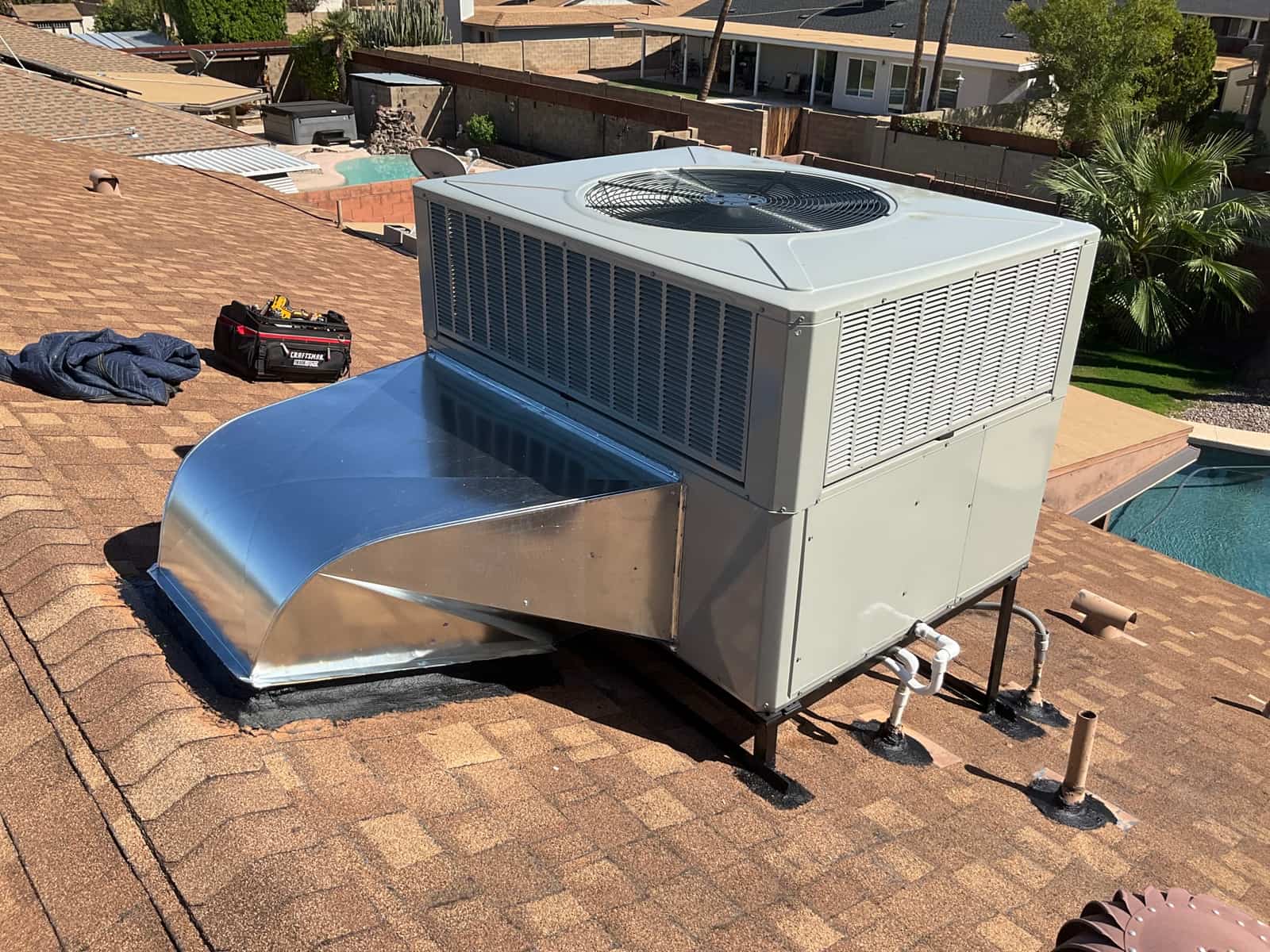 New rooftop package unit installed on a raised stand with sealed curb, connected duct transition, and condensate drain piping.