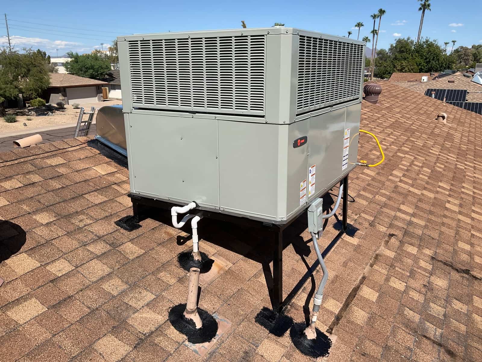 New rooftop package unit set on a raised stand with sealed roof penetrations, condensate drain, electrical whip, and service disconnect.