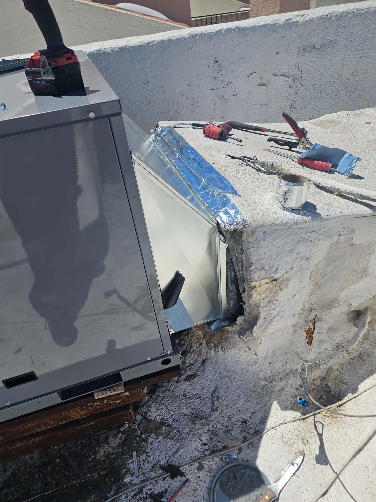 New rooftop package unit set with sheet metal transition and foil-taped duct connection in progress, tools and sealant visible nearby.