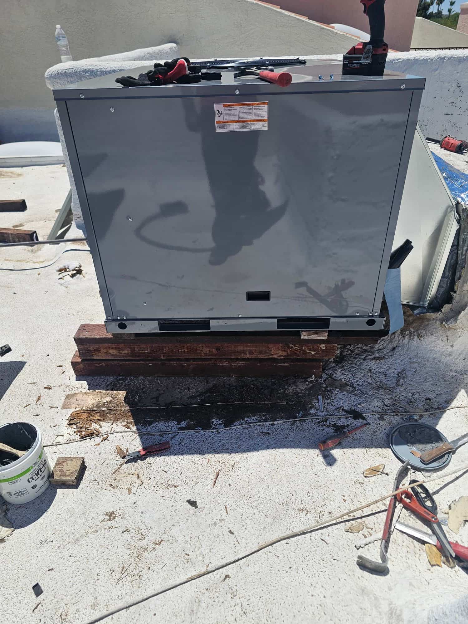 New rooftop package unit set on wood sleepers with tools on top during installation preparation.