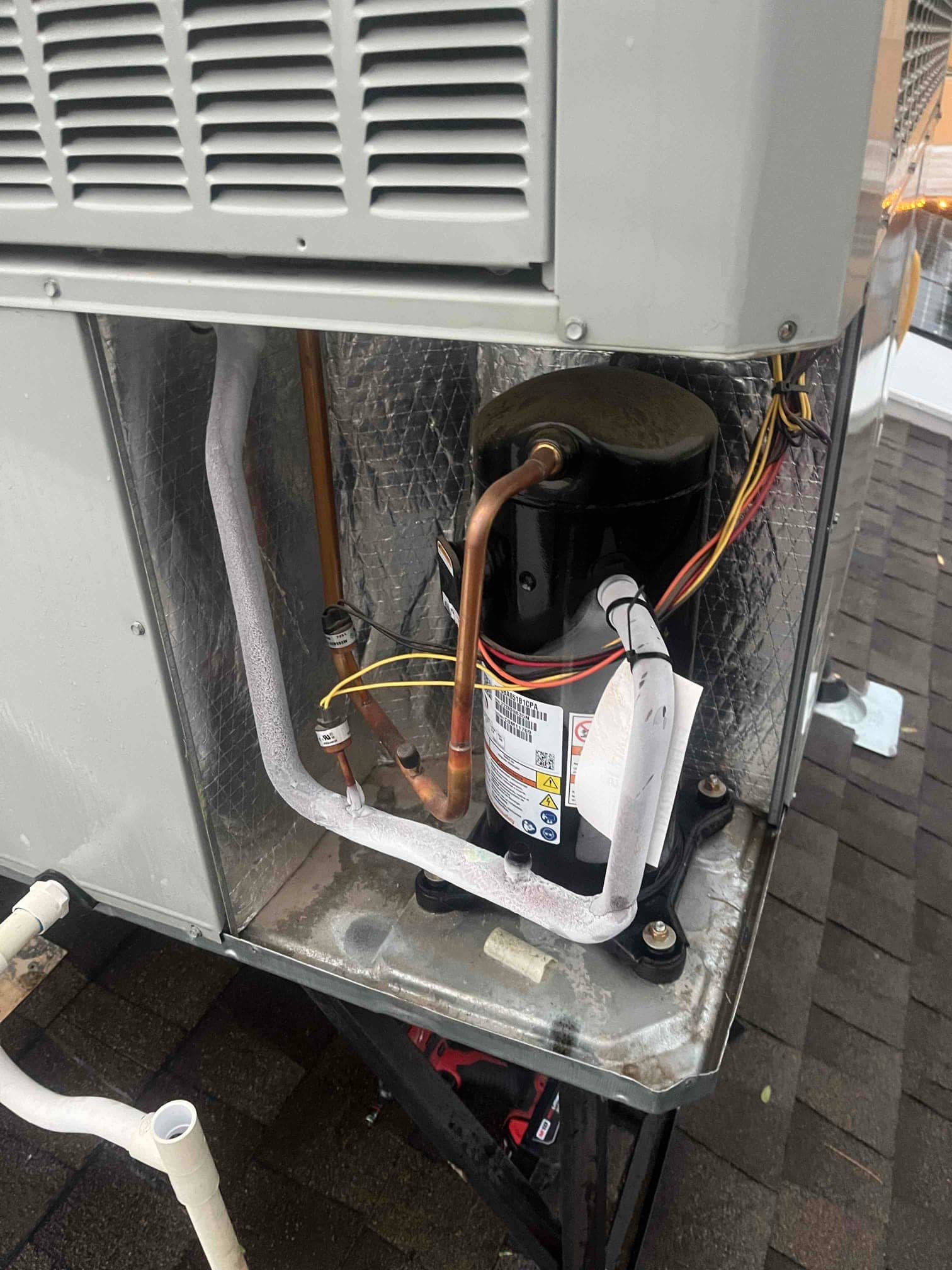 Outdoor condenser compartment open, showing compressor with connected wiring and refrigerant lines, and frost accumulation on the suction line.