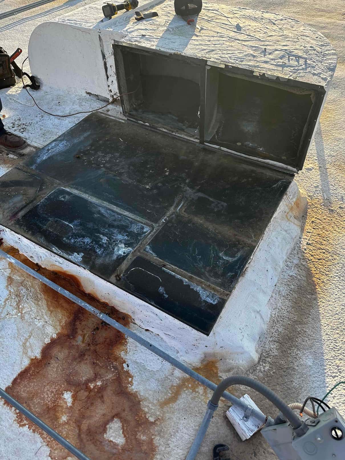 Rooftop curb and duct openings prepared for a new package unit installation, with tools and electrical whip visible nearby.