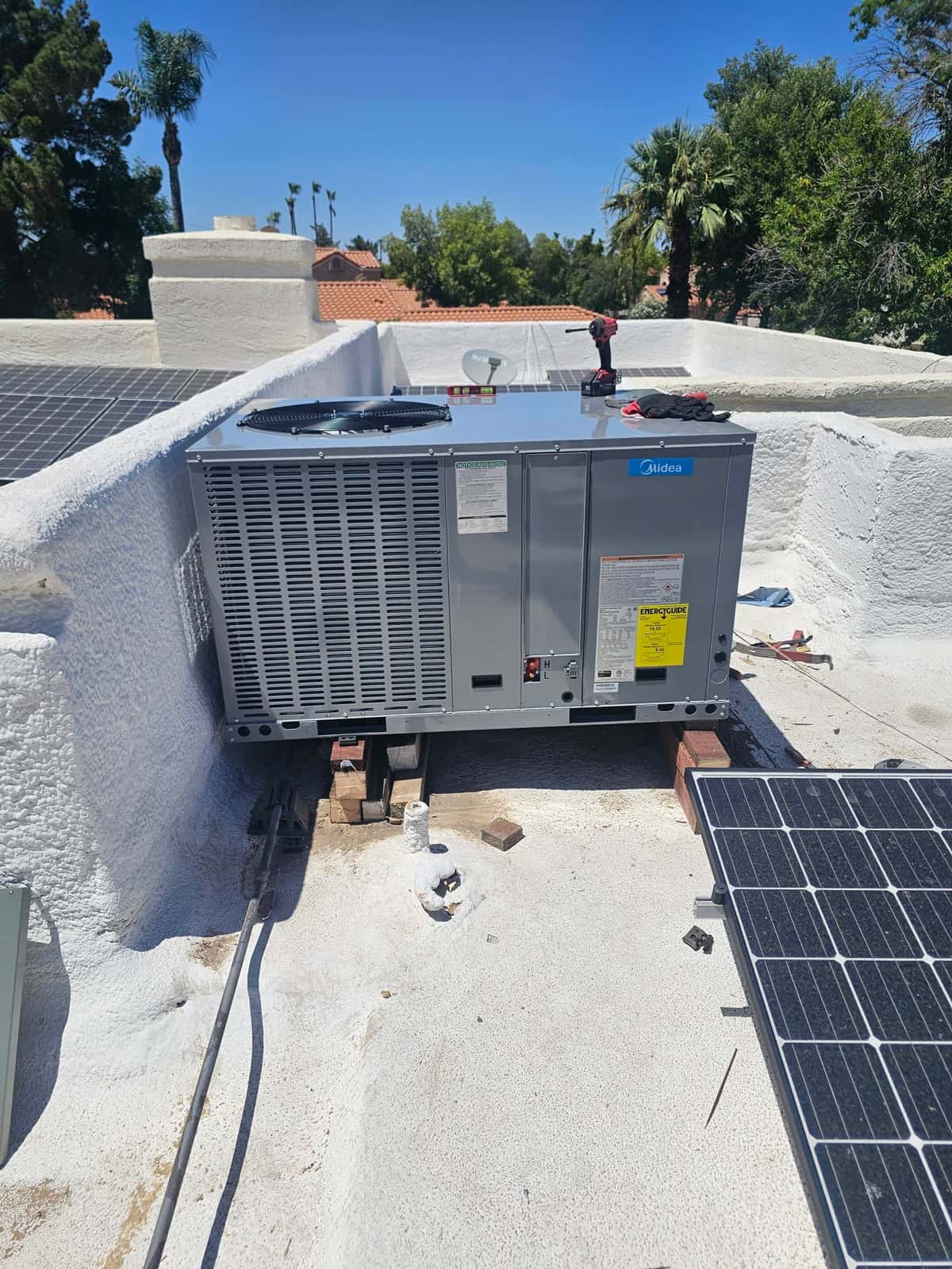 Rooftop package HVAC unit newly set in place on supports, with tools on top and adjacent solar panels visible.