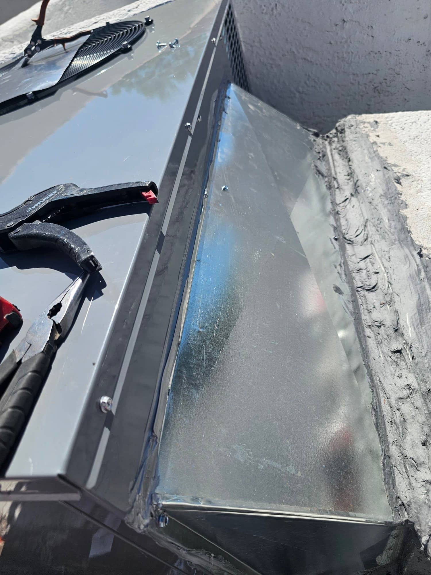 Sheet metal transition duct sealed to a rooftop package unit, with screws and hand tools visible during installation.