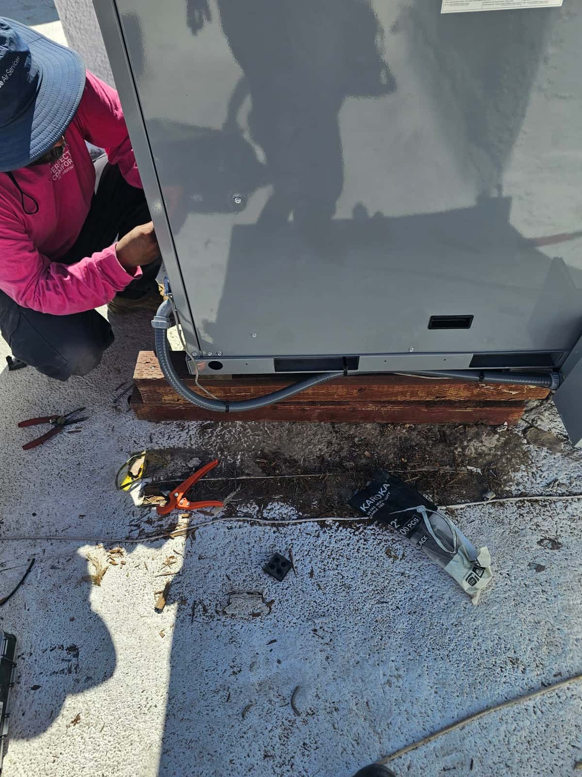 Technician routes flexible electrical conduit and wiring into the new rooftop package unit during installation, with tools and materials nearby.